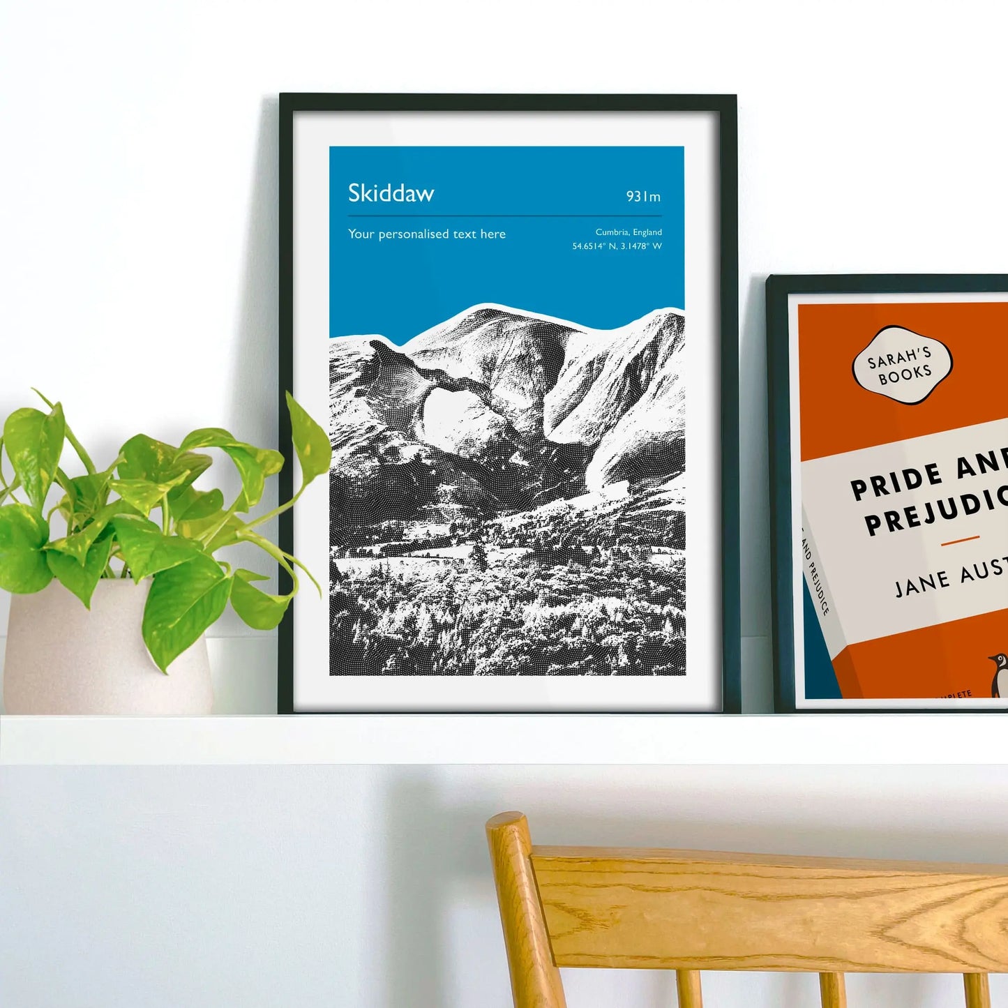 Framed picture on shelf beside a houseplant and another print.