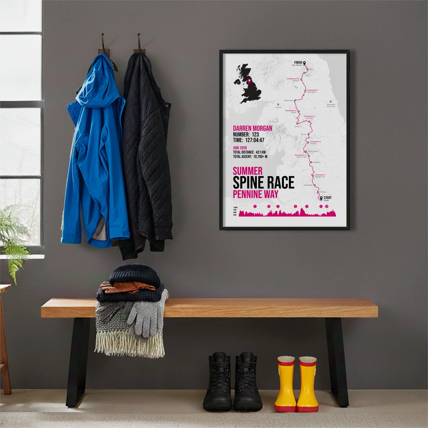 Framed print hanging on grey wall beside coats on hooks above walking boots and shows