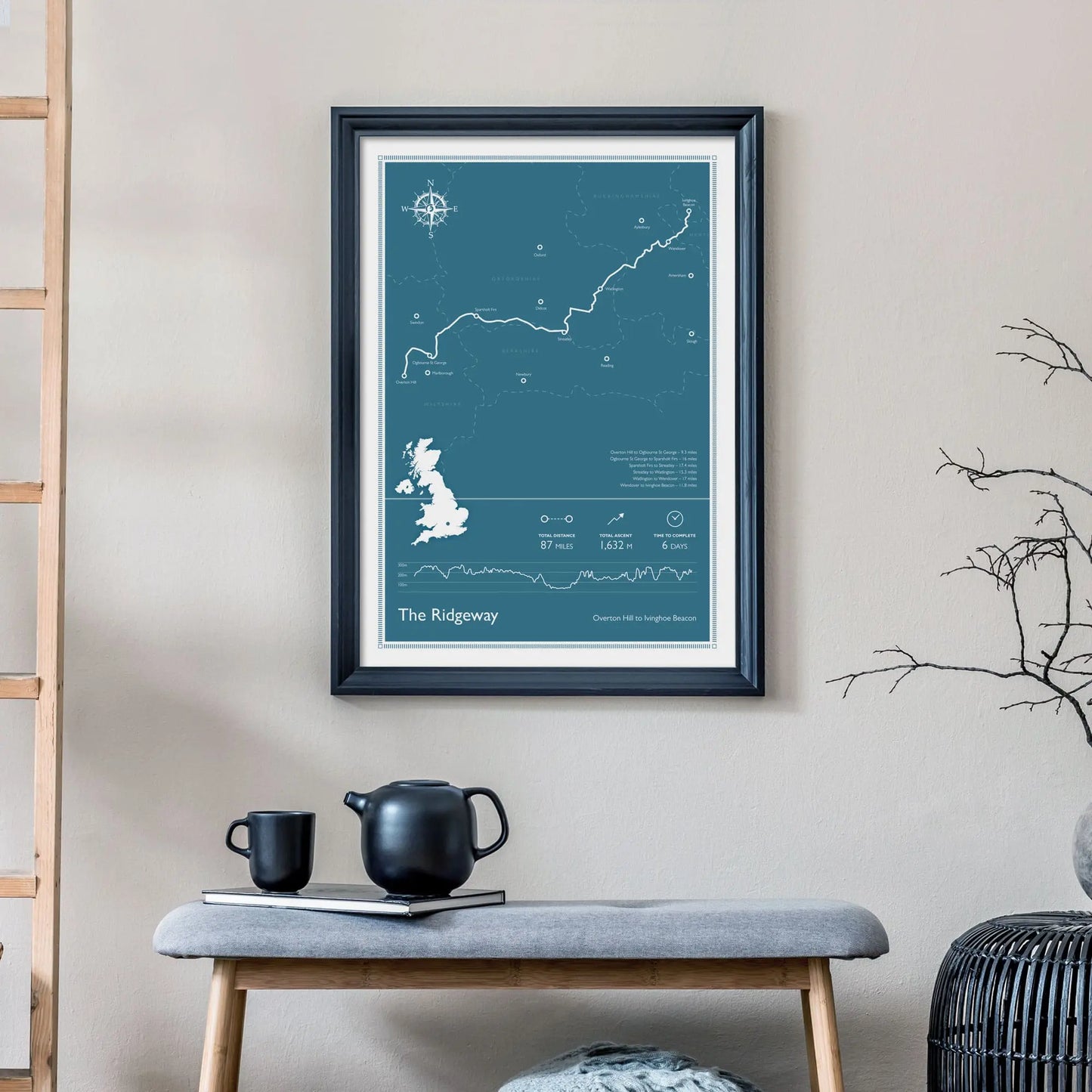 Large Ridgeway National Trail Map print on wall behind a 2 seater sofa covered in cushions with a coffee table covered in books.