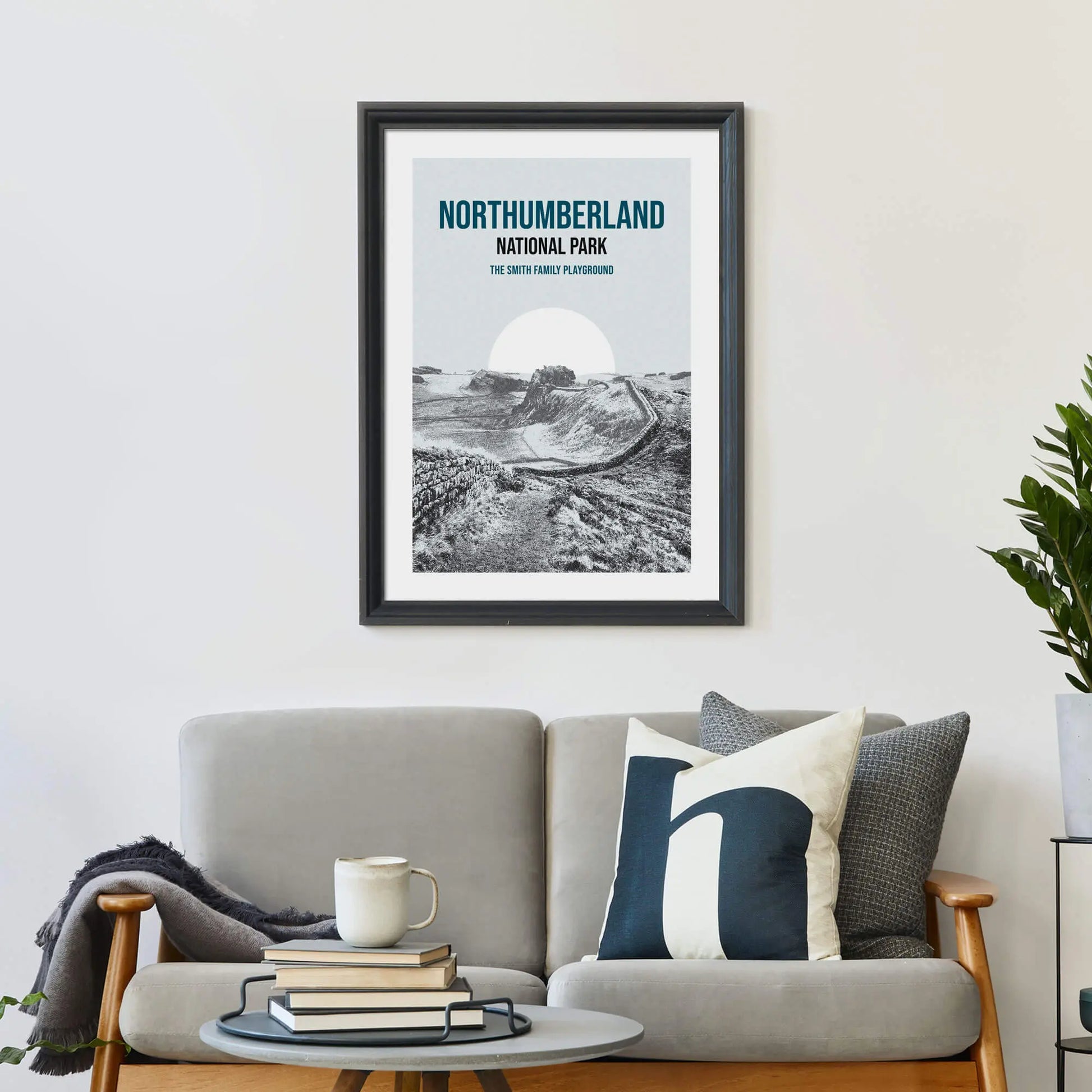 Large print on wall behind a 2 seater sofa covered in cushions with a coffee table covered in books.