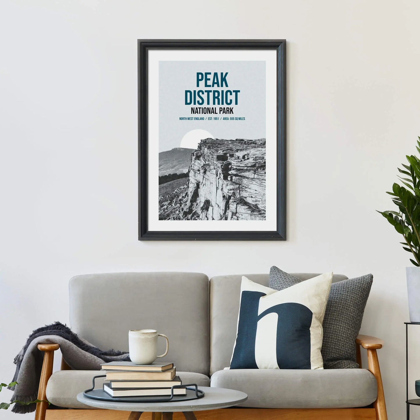 Large print on wall behind a 2 seater sofa covered in cushions with a coffee table covered in books.