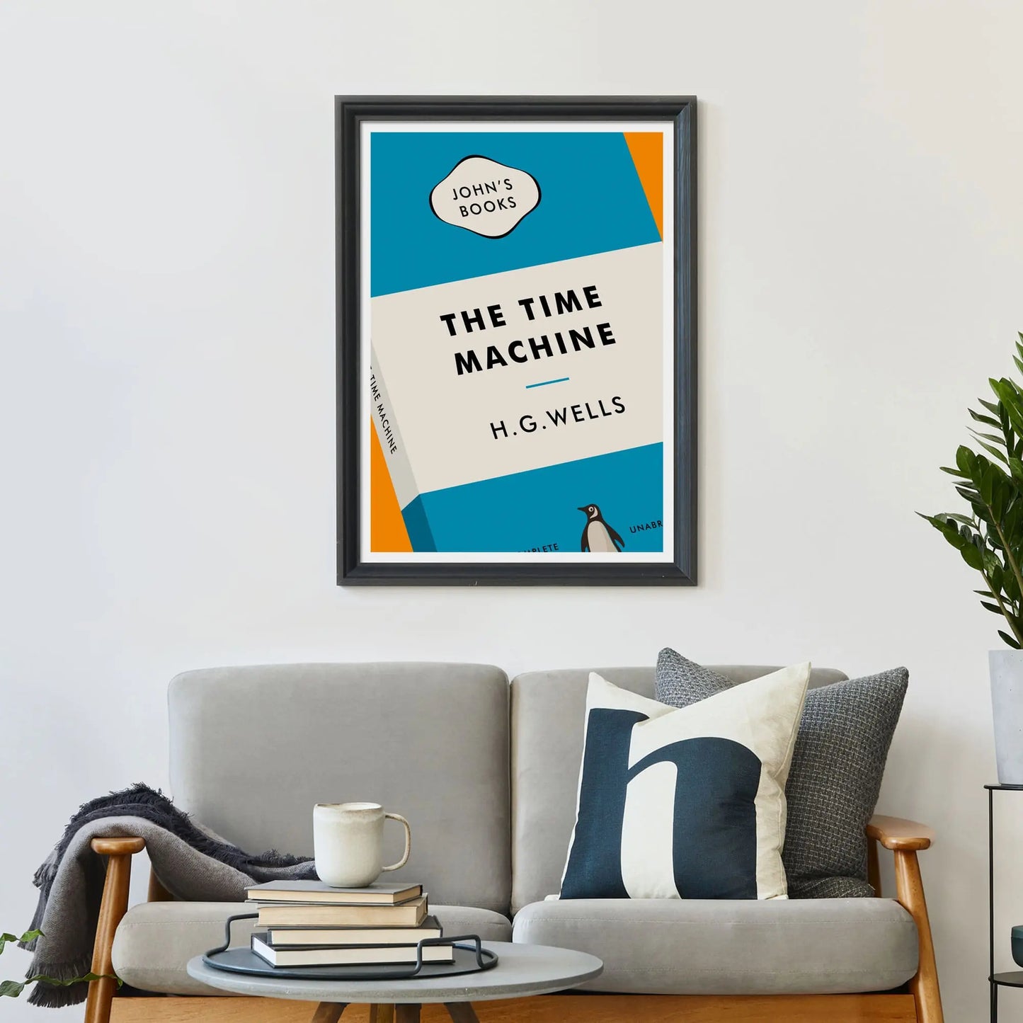 Large print on wall behind a 2 seater sofa covered in cushions with a coffee table covered in books.