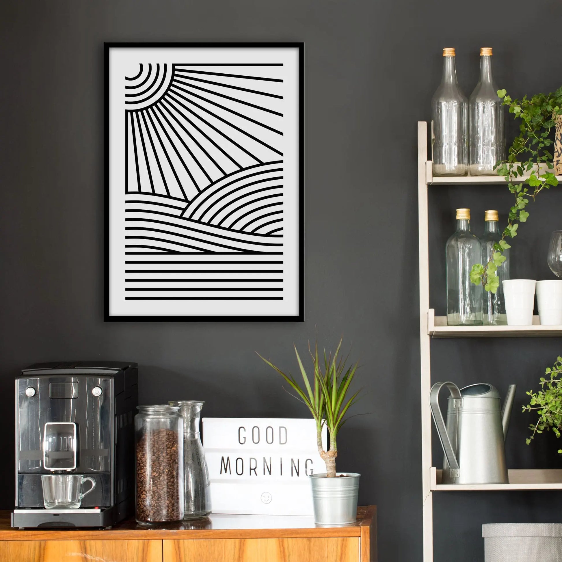 Kitchen wall infront of which is a sideboard with a coffee machine and a set of shelves holding bottles and plants. On the wall above the sideboard is the framed print in a black frame on a dark grey wall.