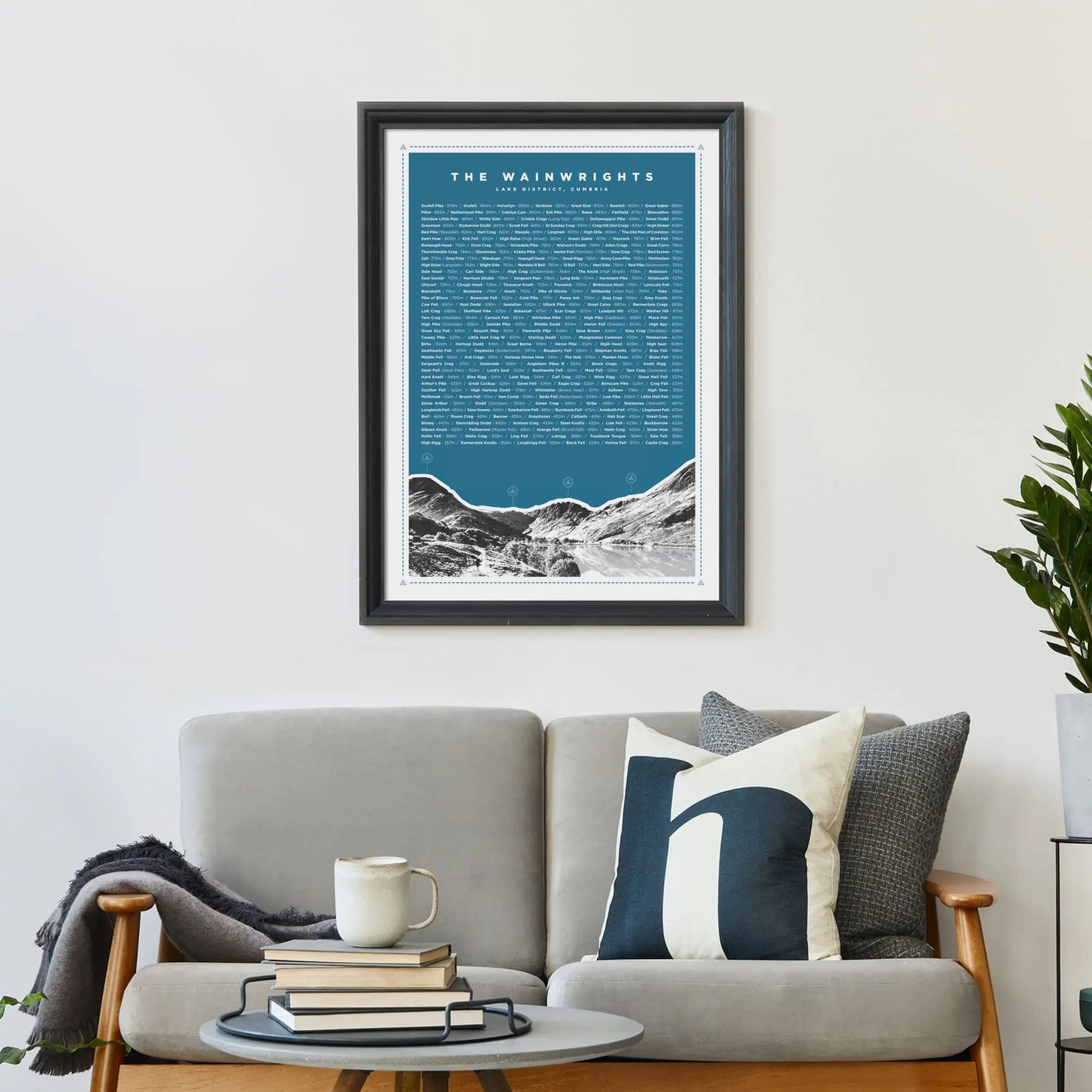 Blue version of the print framed on wall above a sofa covered in cushions with a coffee table in front.