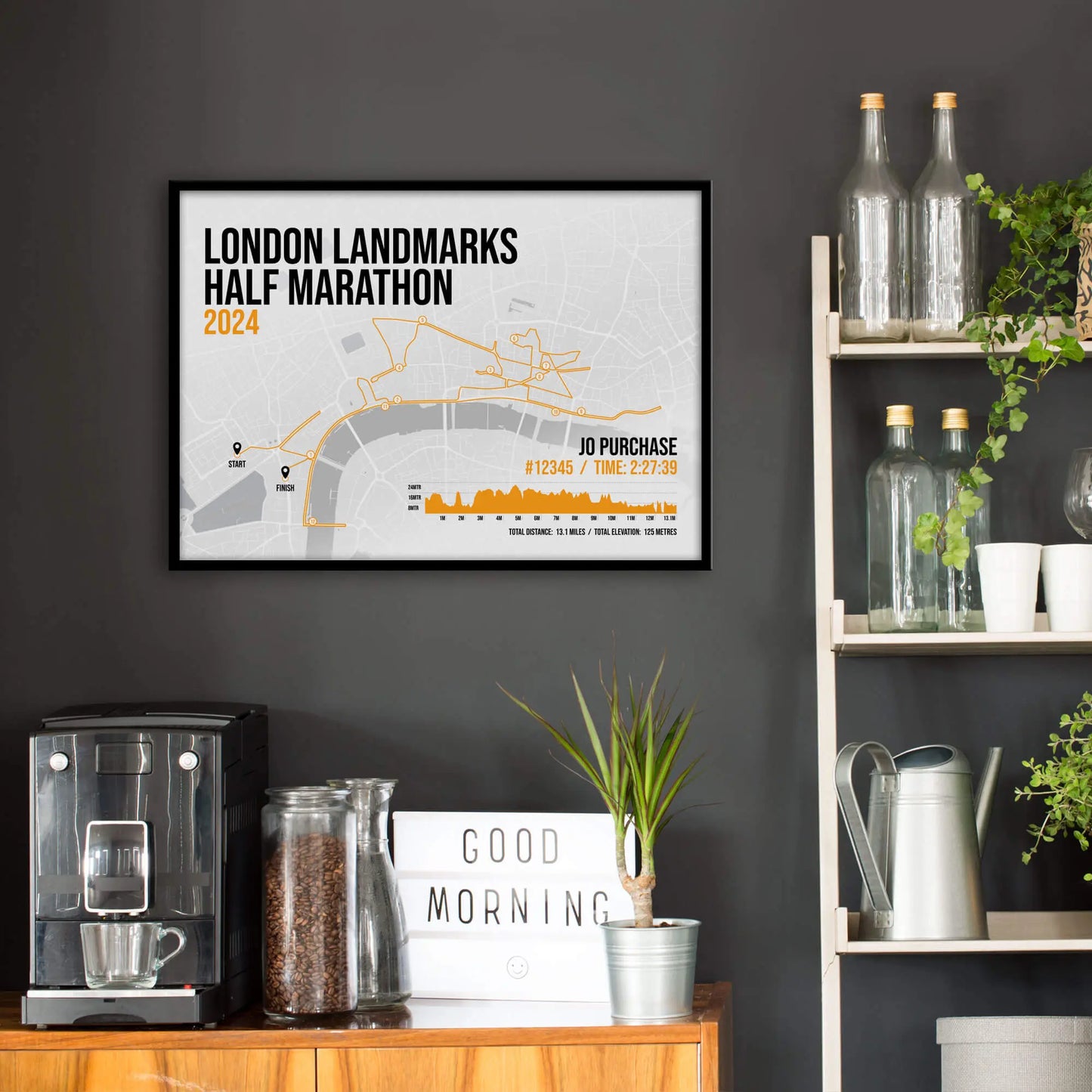 Kitchen wall infront of which is a sideboard with a coffee machine and a set of shelves holding bottles and plants. On the wall above the sideboard is the framed print in a black frame on a dark grey wall.