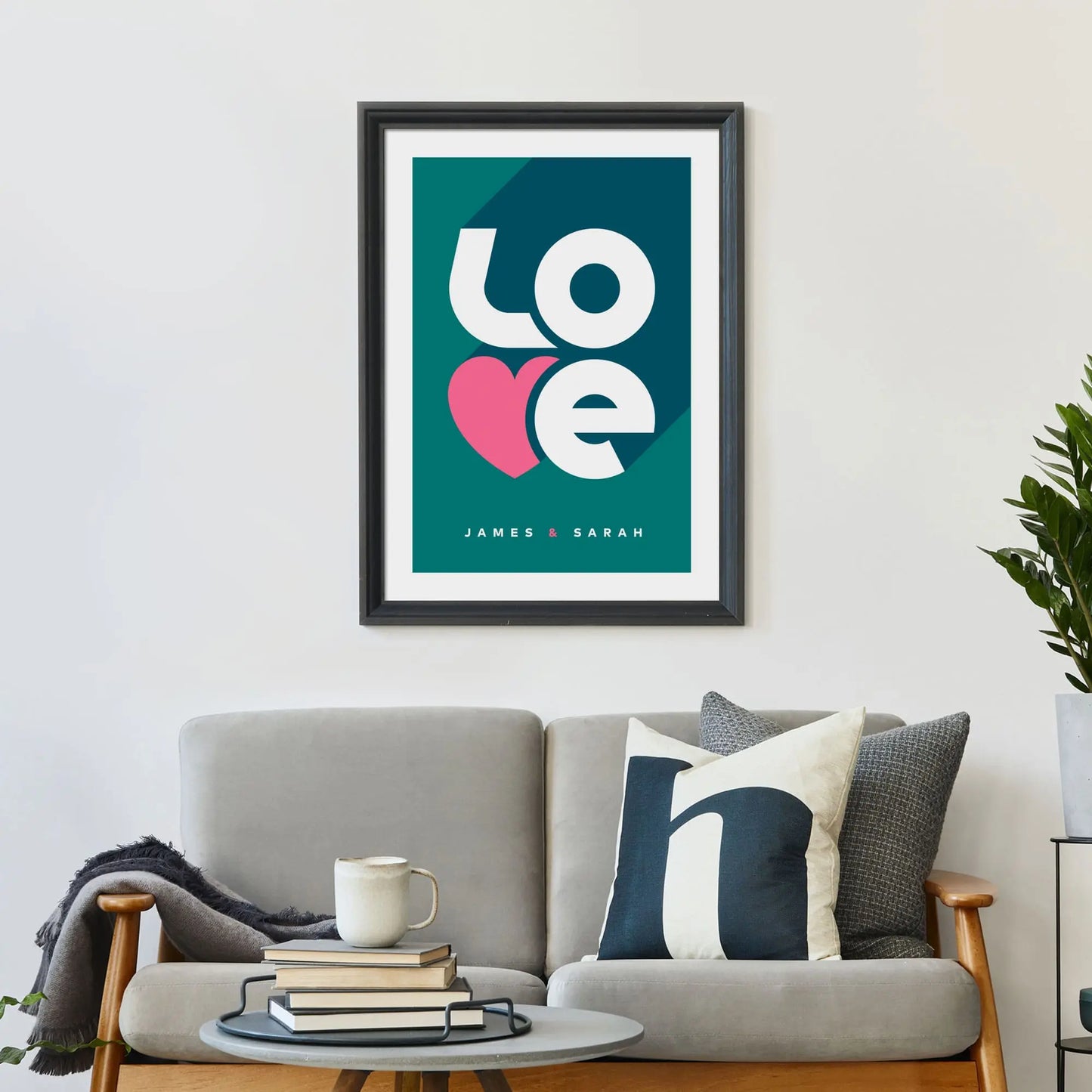 Large print on wall behind a 2 seater sofa covered in cushions with a coffee table covered in books.