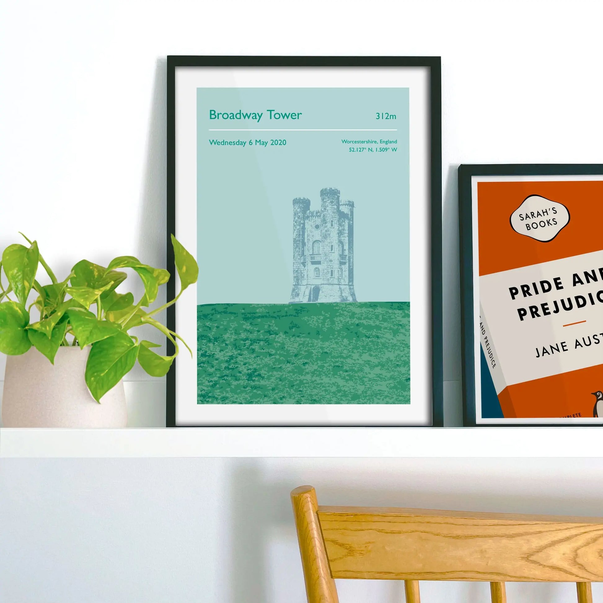 Framed picture on shelf beside a houseplant and another print.