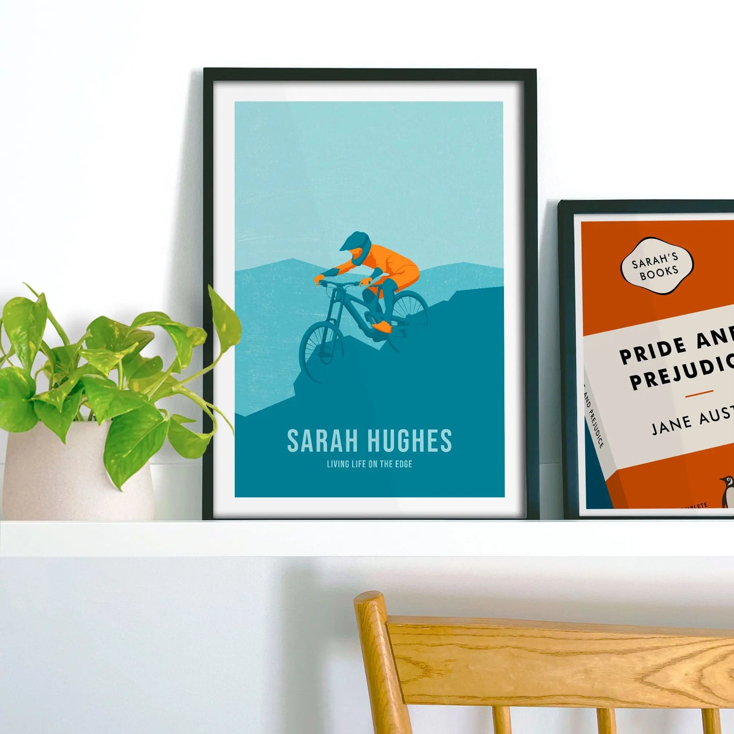 Framed picture on shelf beside a houseplant and another print.