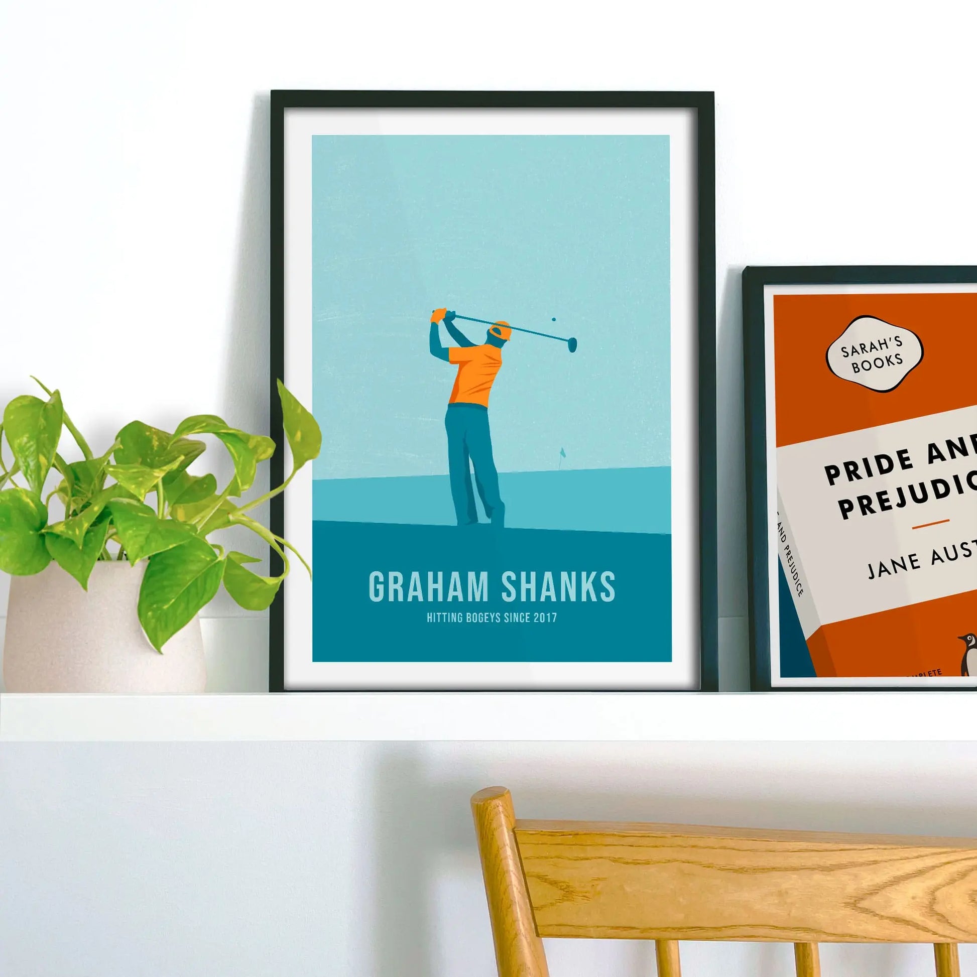 Framed picture on shelf beside a houseplant and another print.