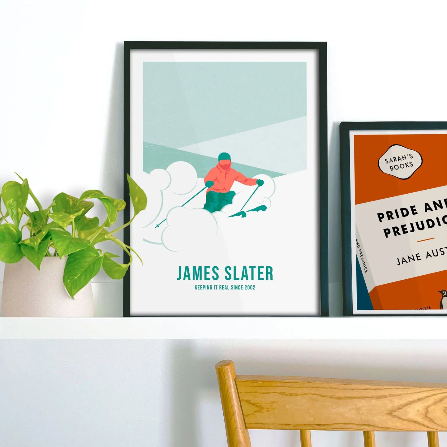 Framed picture on shelf beside a houseplant and another print.