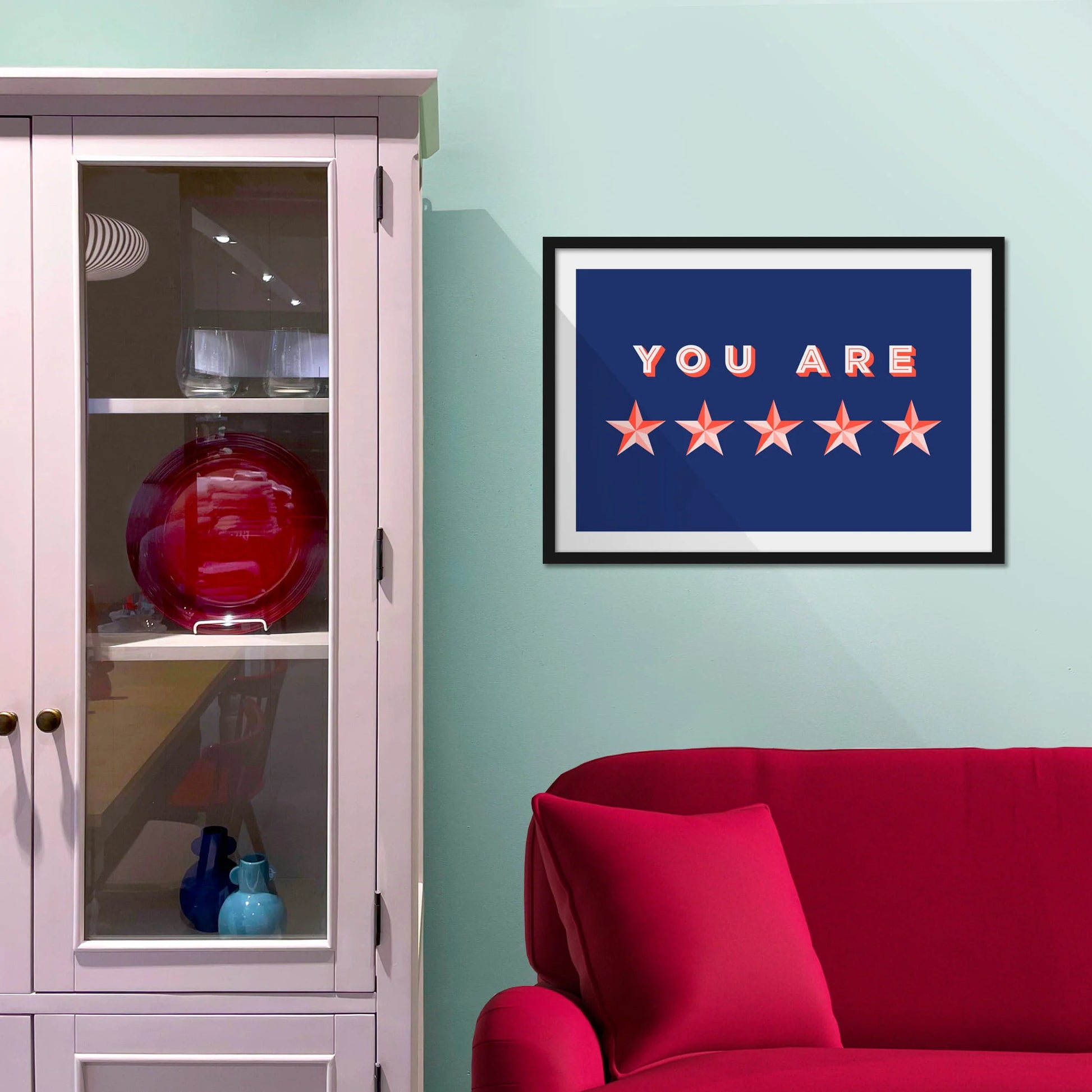Framed picture on blue wall beside shelves above a red sofa