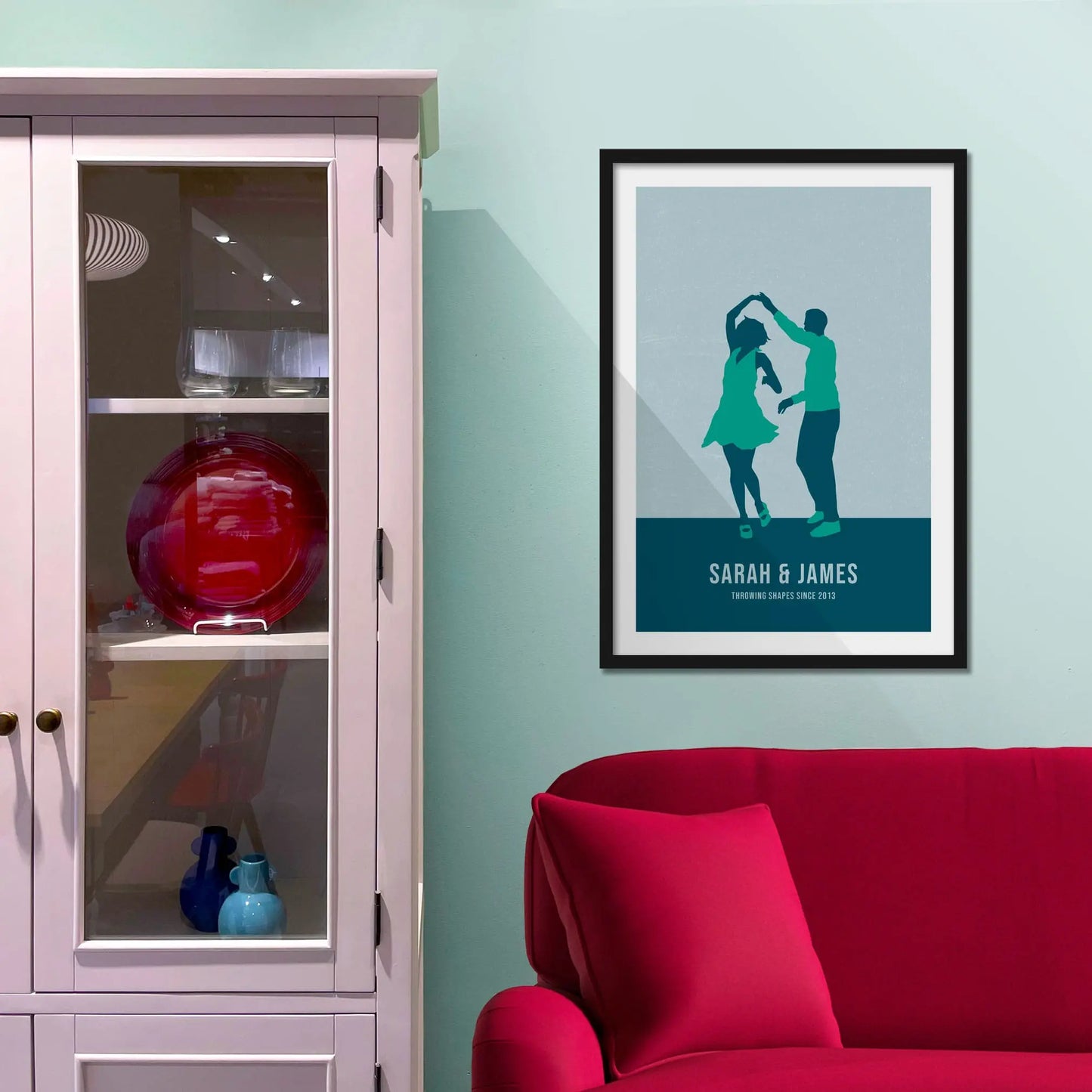 Framed picture on a baby blue wall beside pink shelving