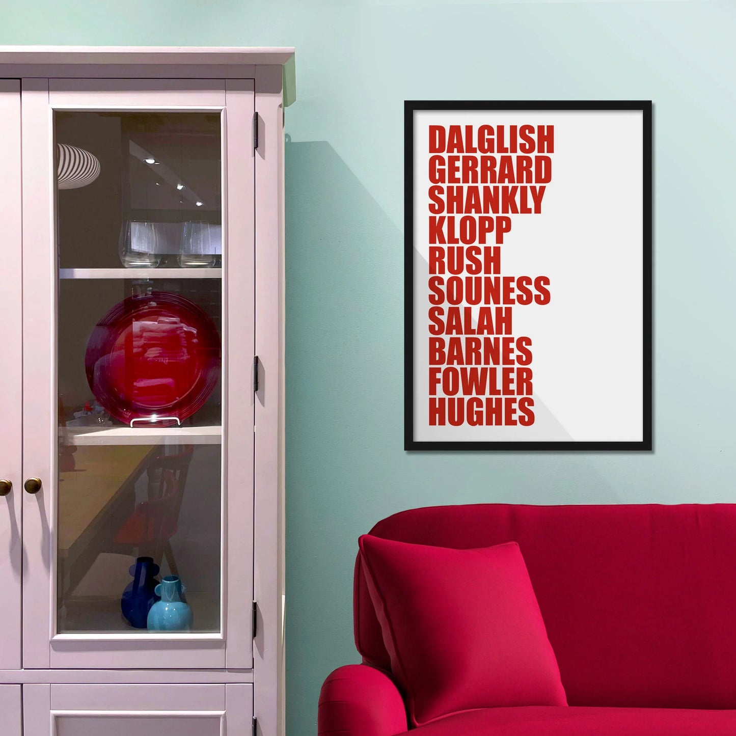 Framed picture on blue wall beside shelves above a red sofa