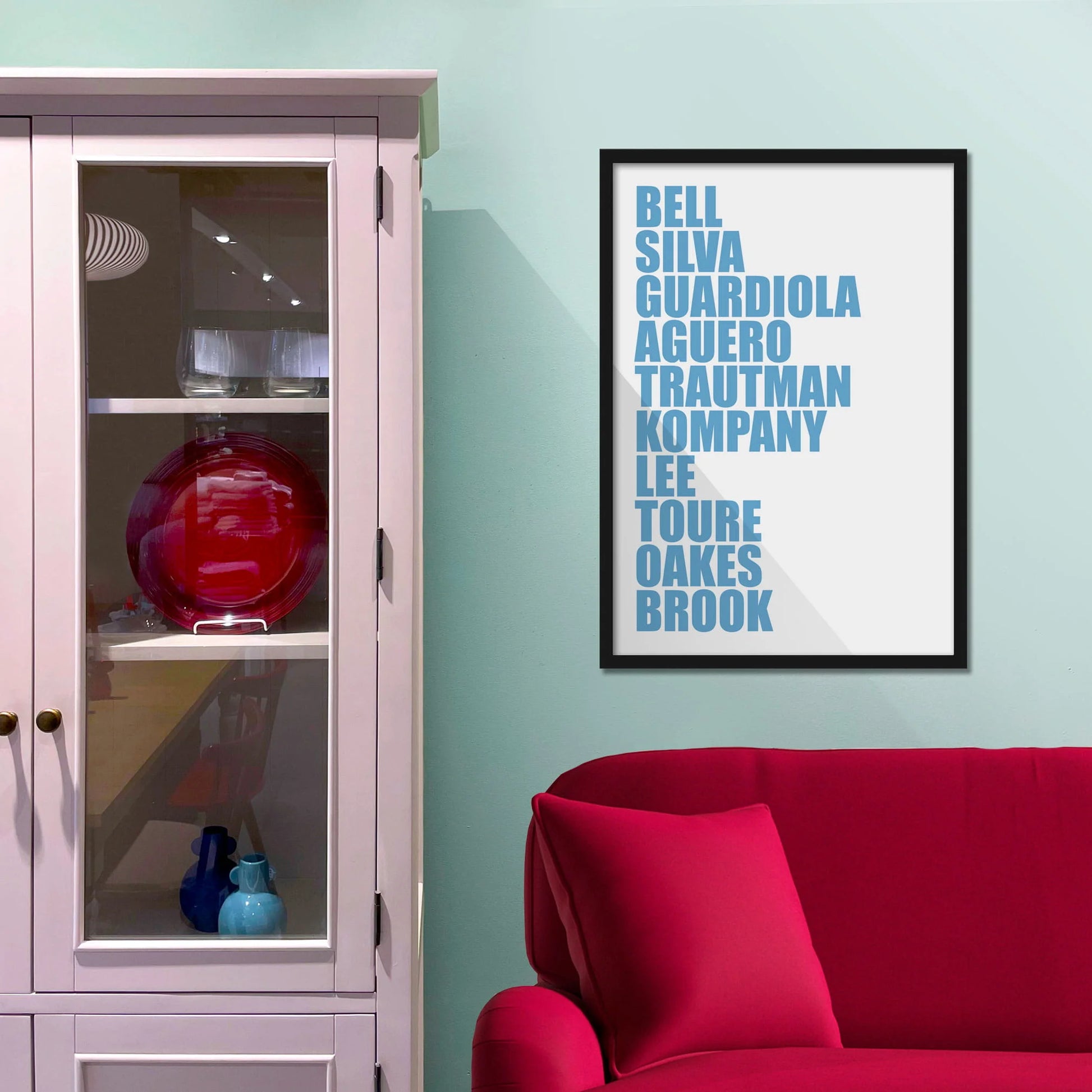 Framed picture on blue wall beside shelves above a red sofa