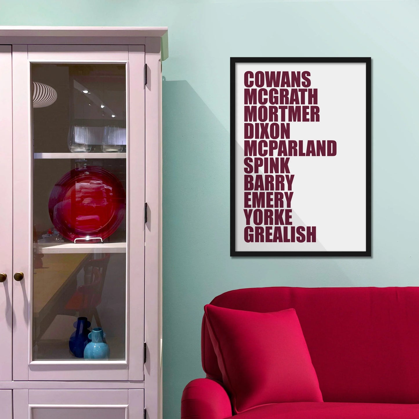 Framed picture on blue wall beside shelves above a red sofa