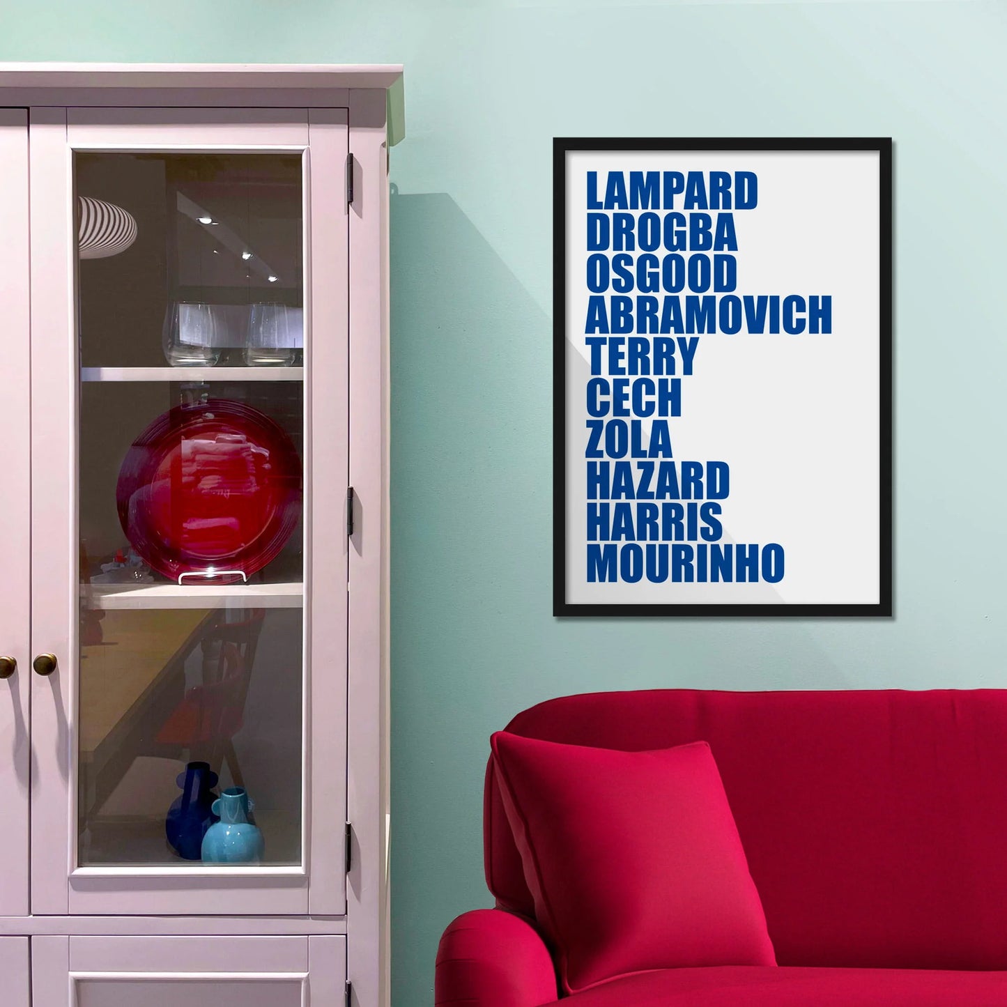 Framed picture on blue wall beside shelves above a red sofa