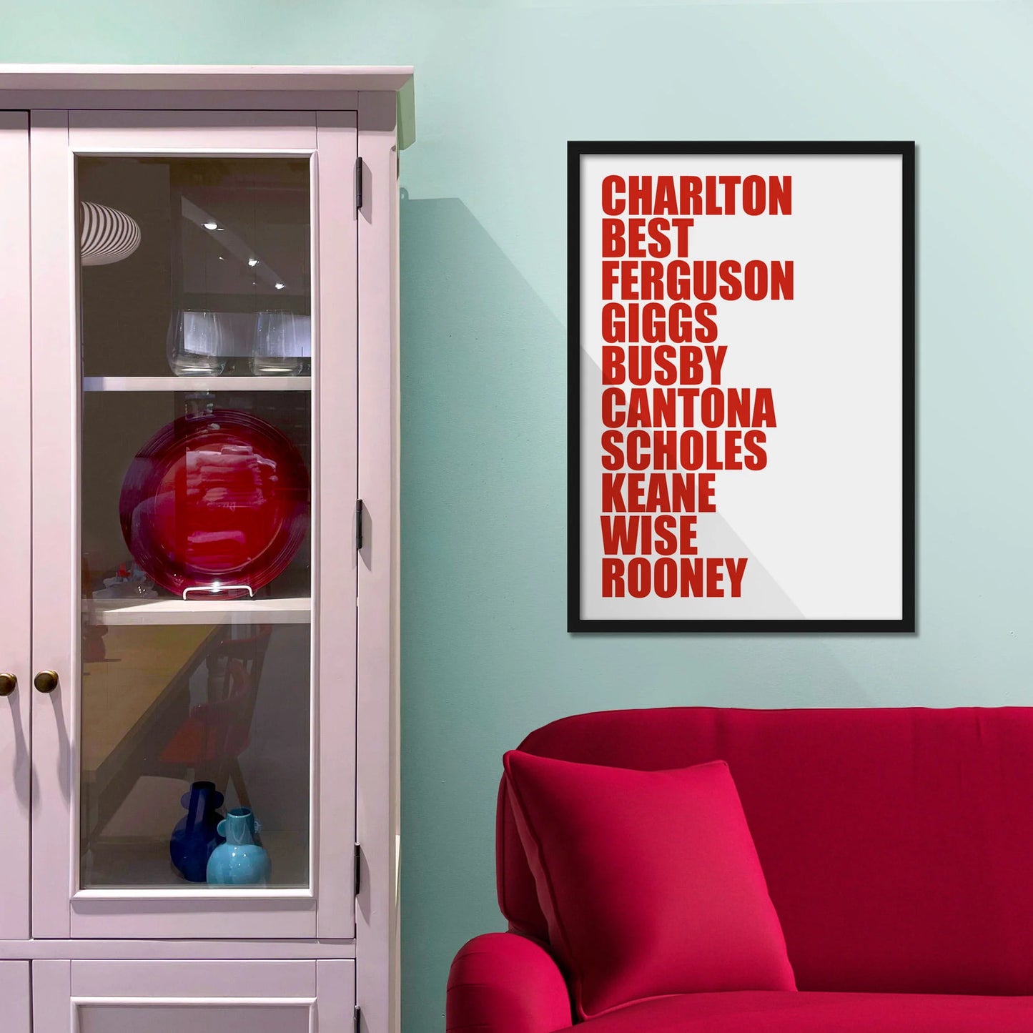 Framed picture on blue wall beside shelves above a red sofa