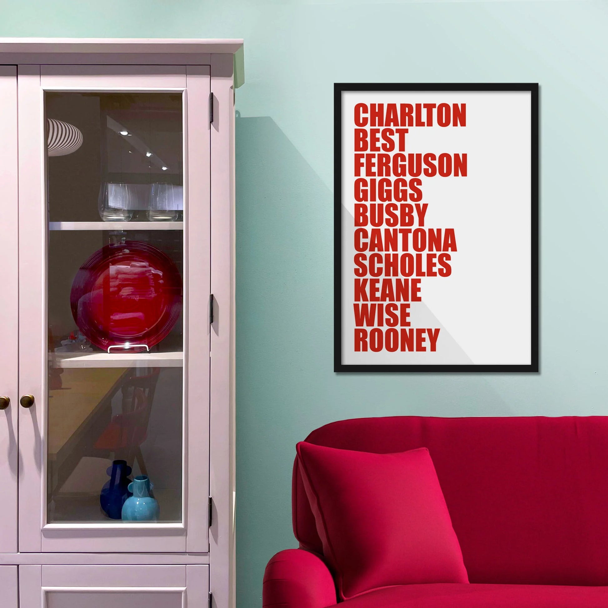 Framed picture on blue wall beside shelves above a red sofa