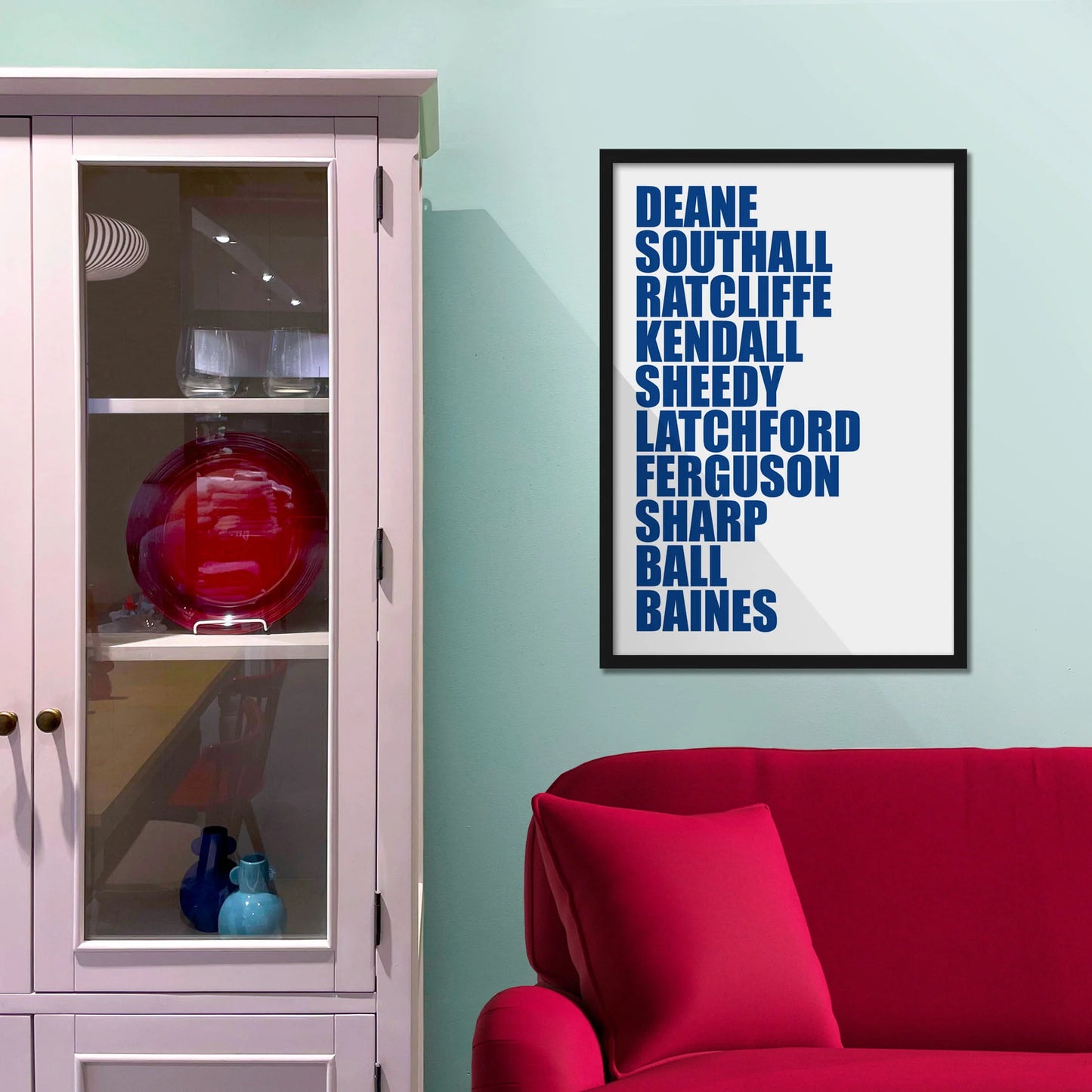 Framed picture on blue wall beside shelves above a red sofa