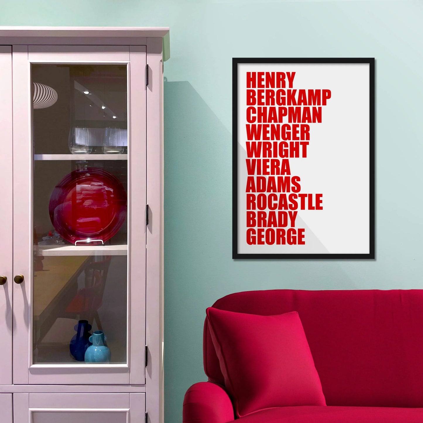 Framed picture on blue wall beside shelves above a red sofa