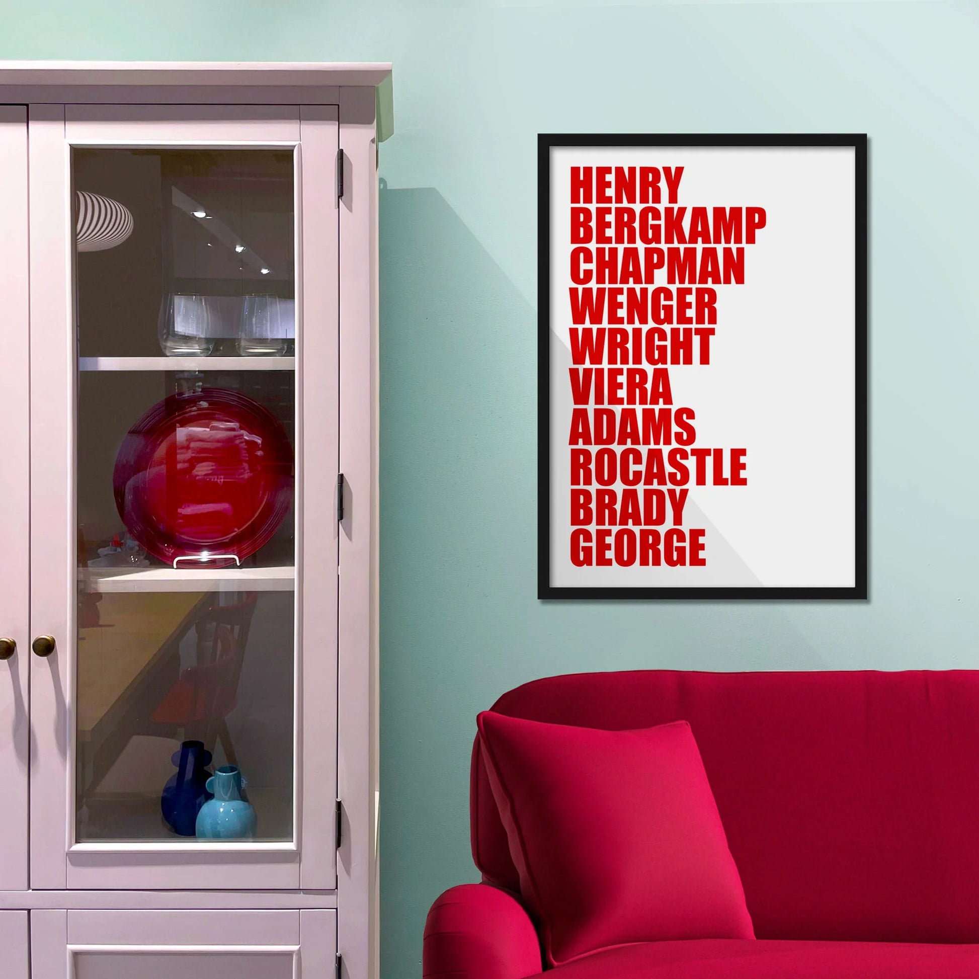 Framed picture on blue wall beside shelves above a red sofa