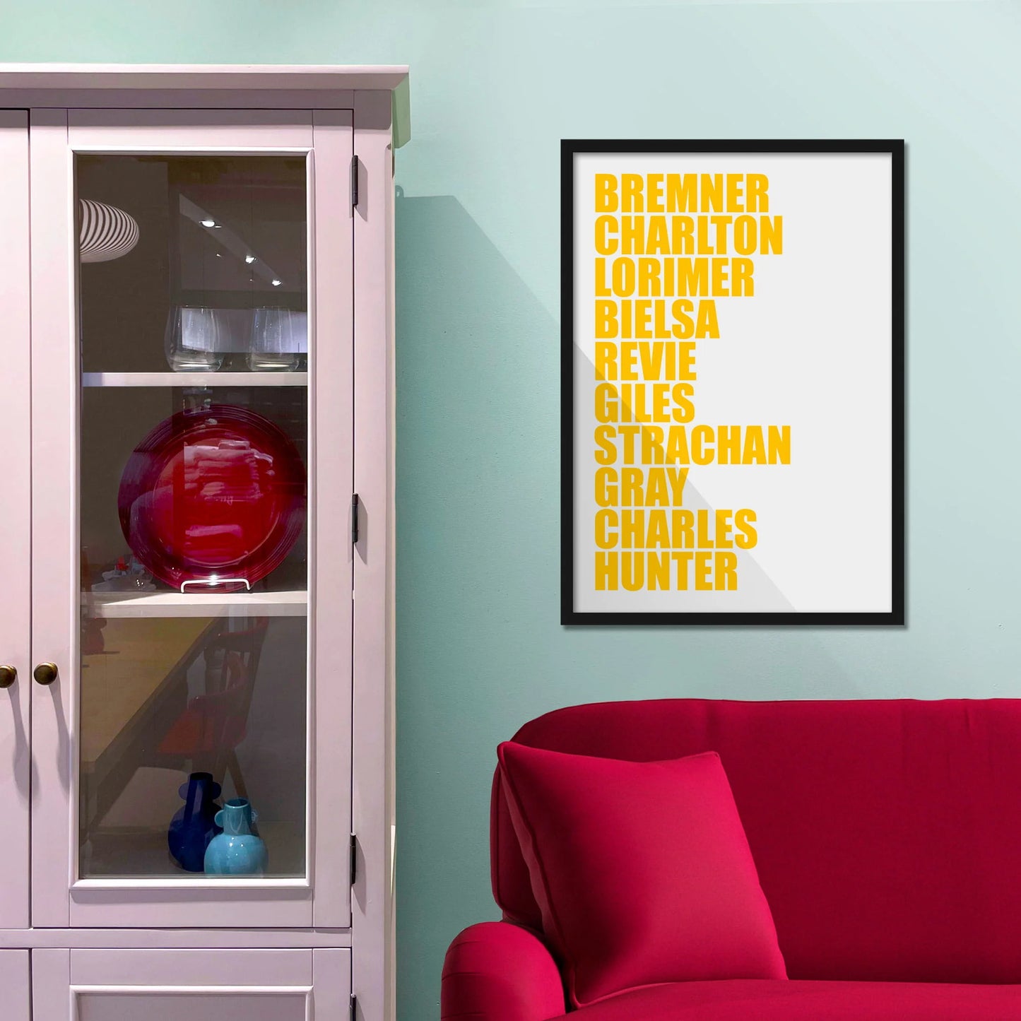 Framed picture on blue wall beside shelves above a red sofa