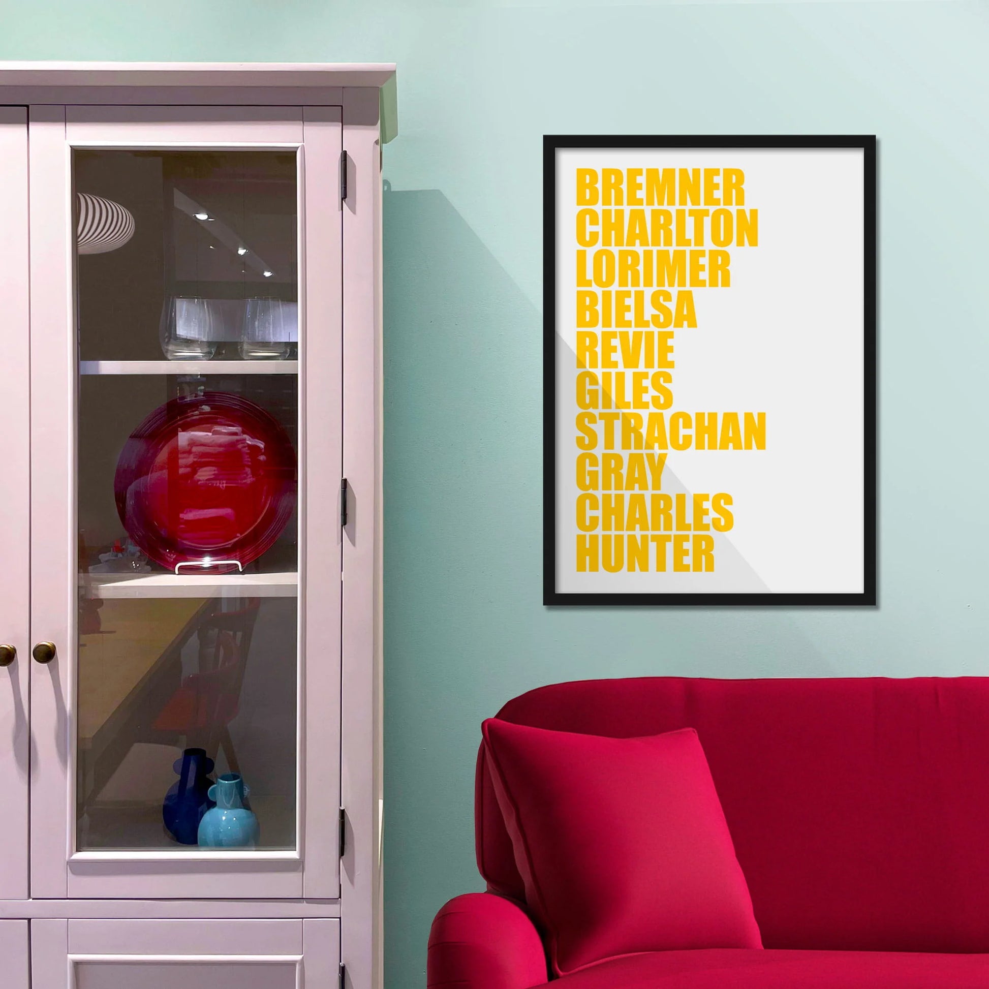Framed picture on blue wall beside shelves above a red sofa