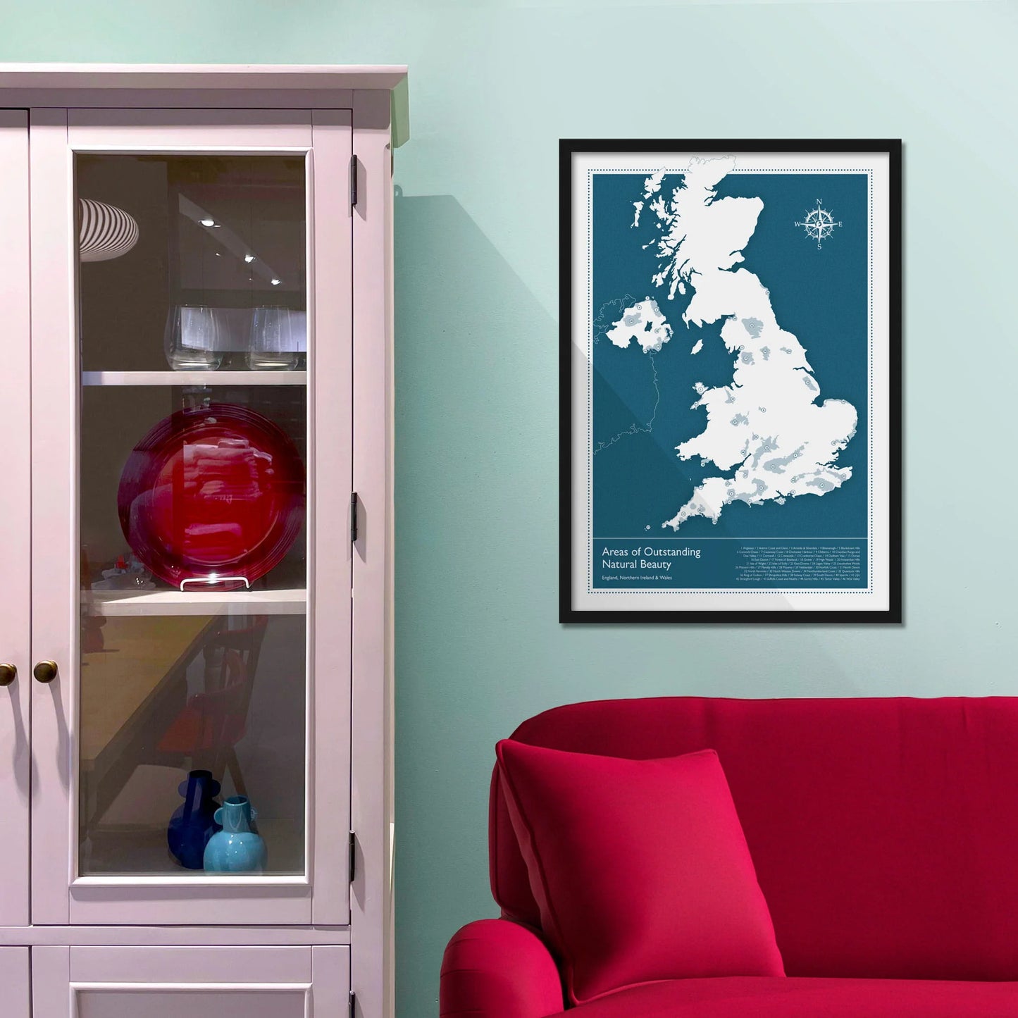 Framed picture on blue wall beside shelves above a red sofa