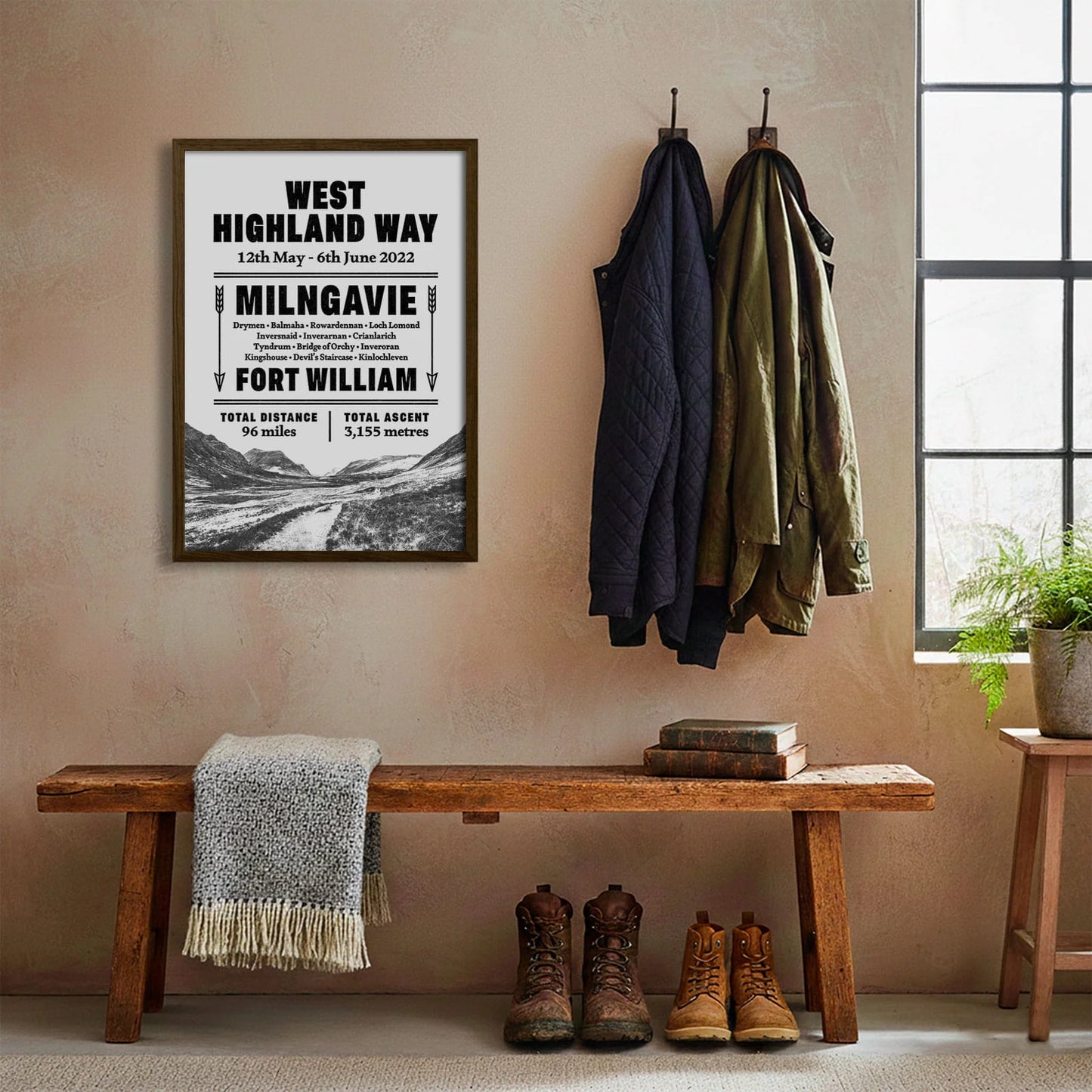 Framed print hanging on cream wall beside coats hanging above bench with walking boots and a scarf