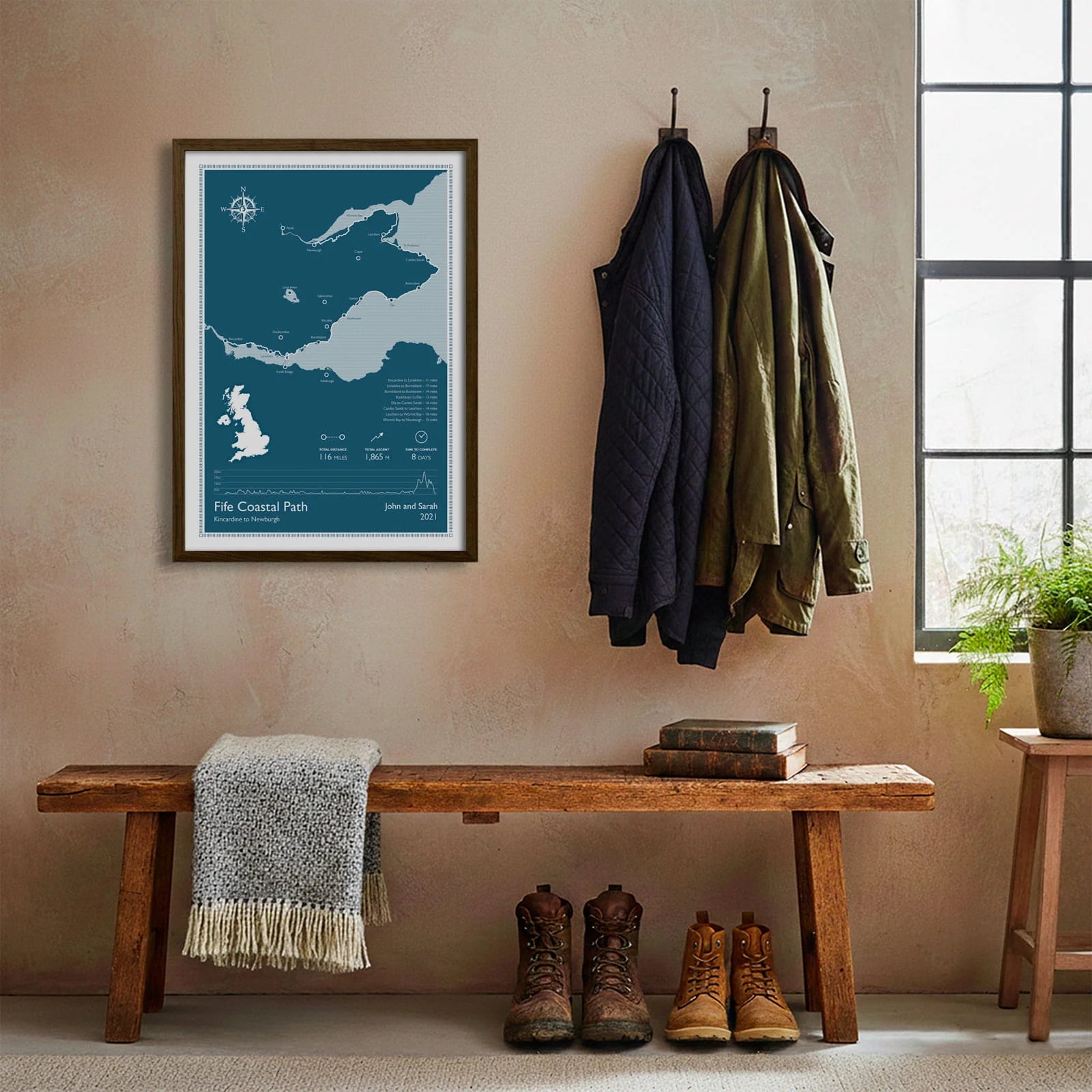 Framed print hanging on cream wall beside coats hanging above bench with walking boots and a scarf