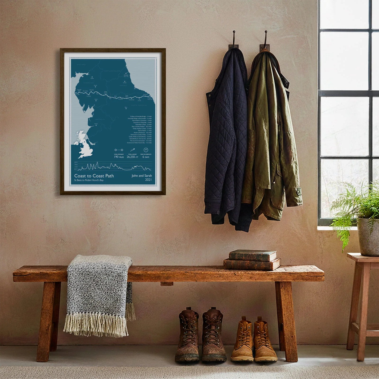 Framed print hanging on cream wall beside coats hanging above bench with walking boots and a scarf