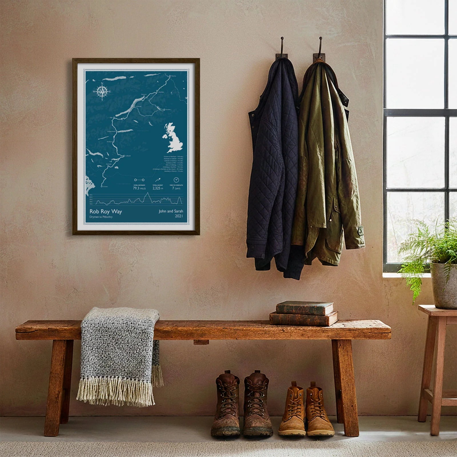 Framed print hanging on cream wall beside coats hanging above bench with walking boots and a scarf