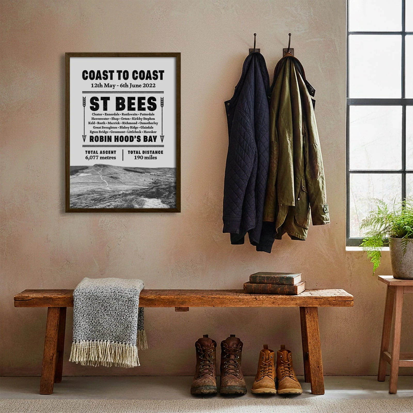 Framed print hanging on cream wall beside coats hanging above bench with walking boots and a scarf
