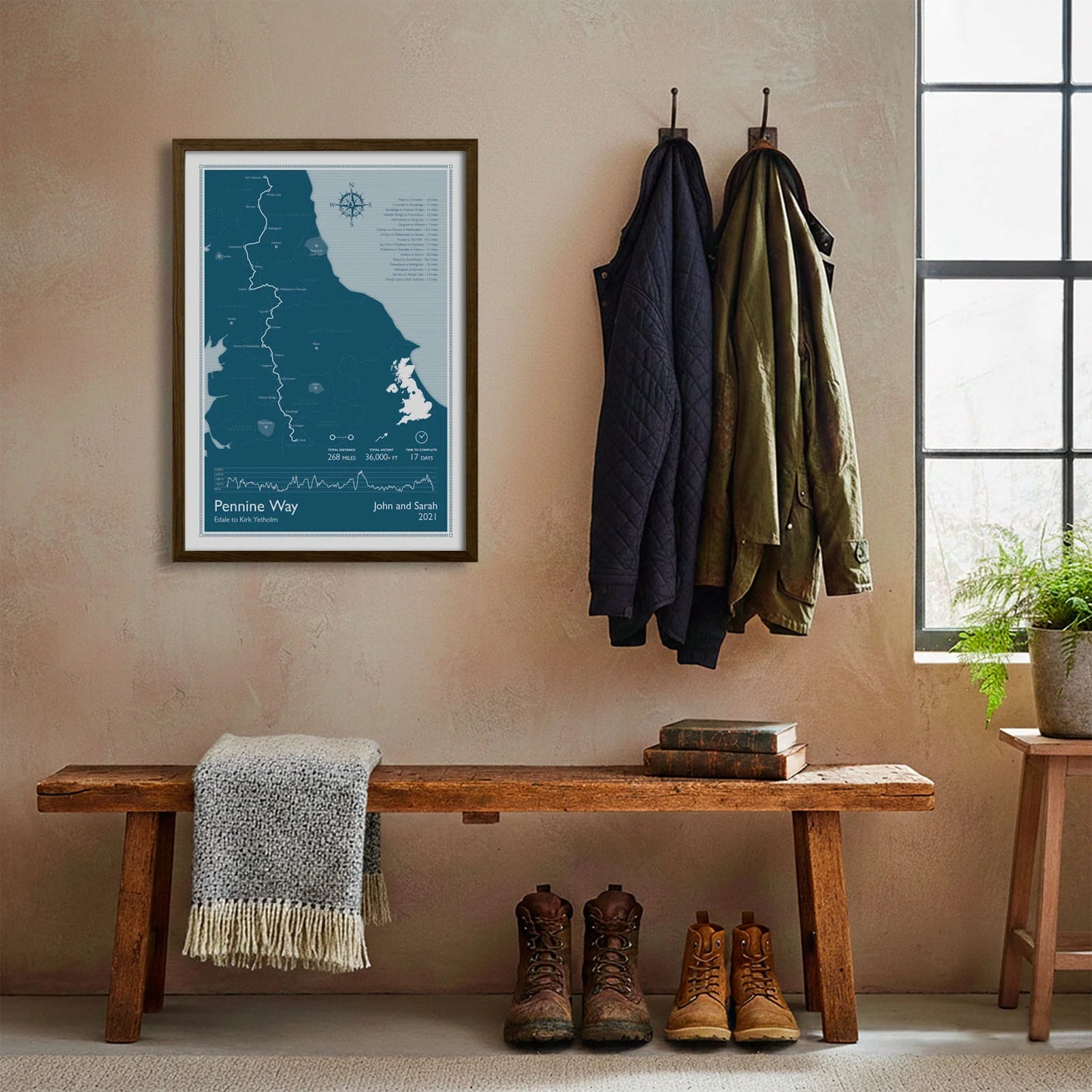 Framed print hanging on cream wall beside coats hanging above bench with walking boots and a scarf