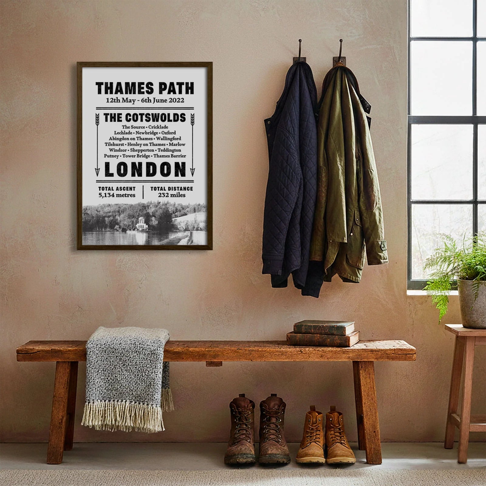 Framed print hanging on cream wall beside coats hanging above bench with walking boots and a scarf