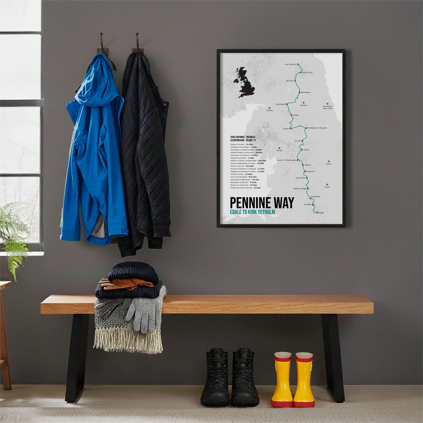 Framed print hanging on grey wall beside coats hanging above bench with walking boots and a scarf