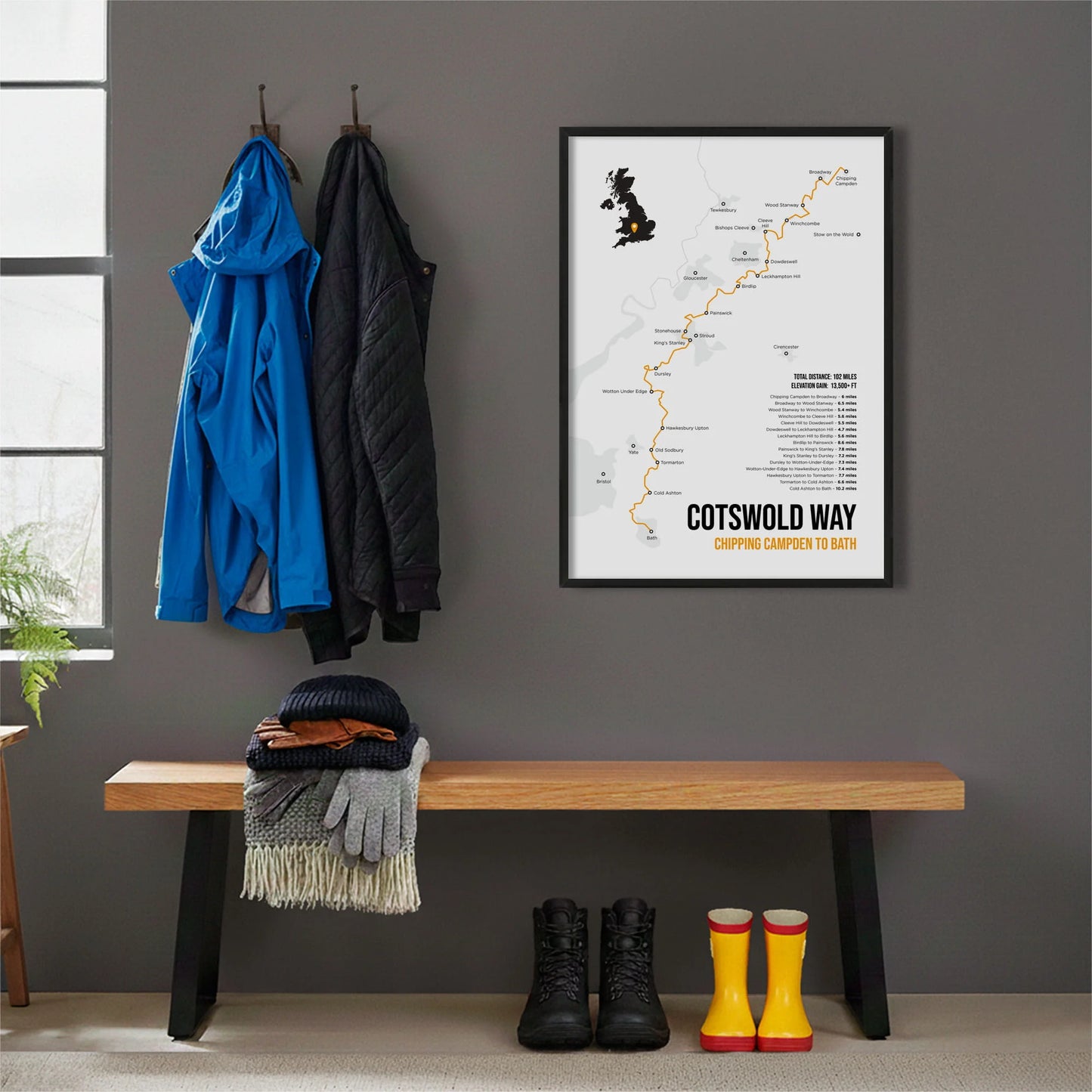 Framed print hanging on grey wall beside coats hanging above bench with walking boots and a scarf