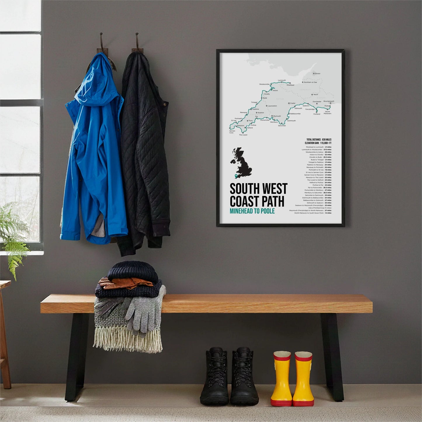 Framed print hanging on grey wall beside coats hanging above bench with walking boots and a scarf