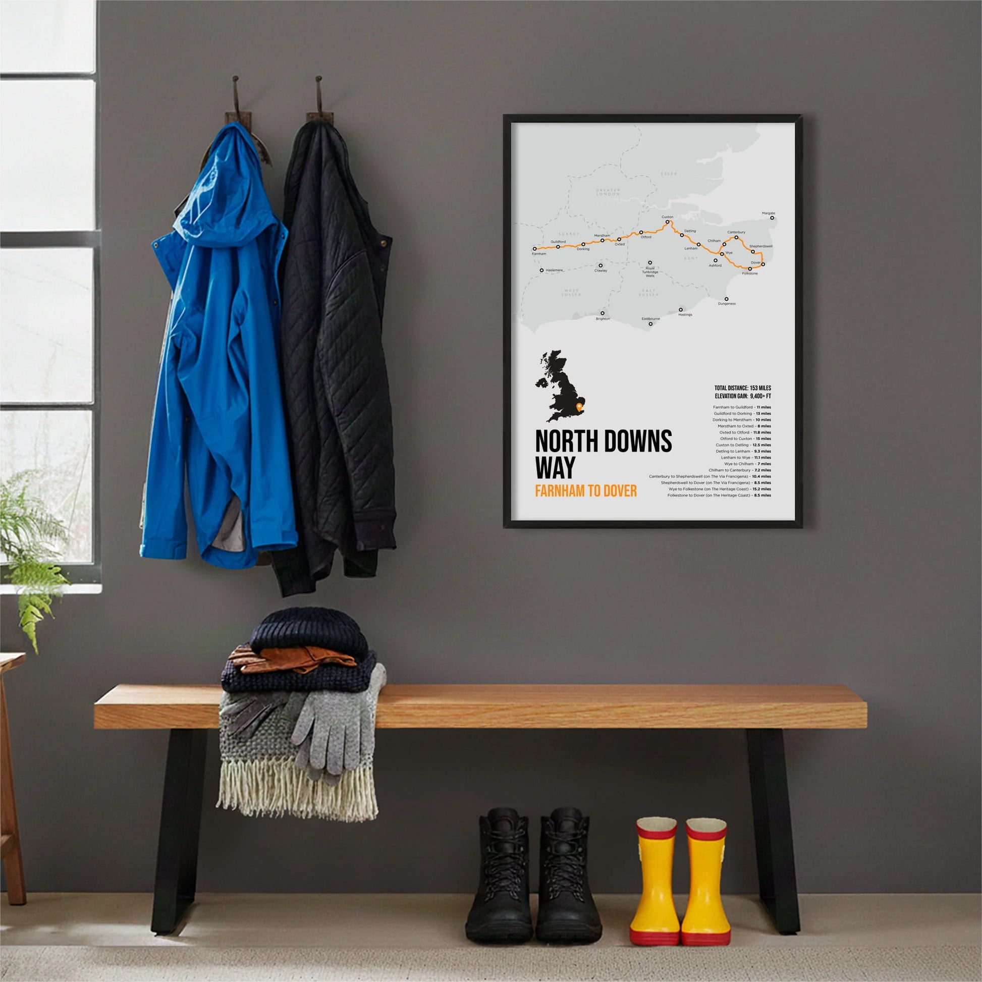 Framed print hanging on grey wall beside coats hanging above bench with walking boots and a scarf