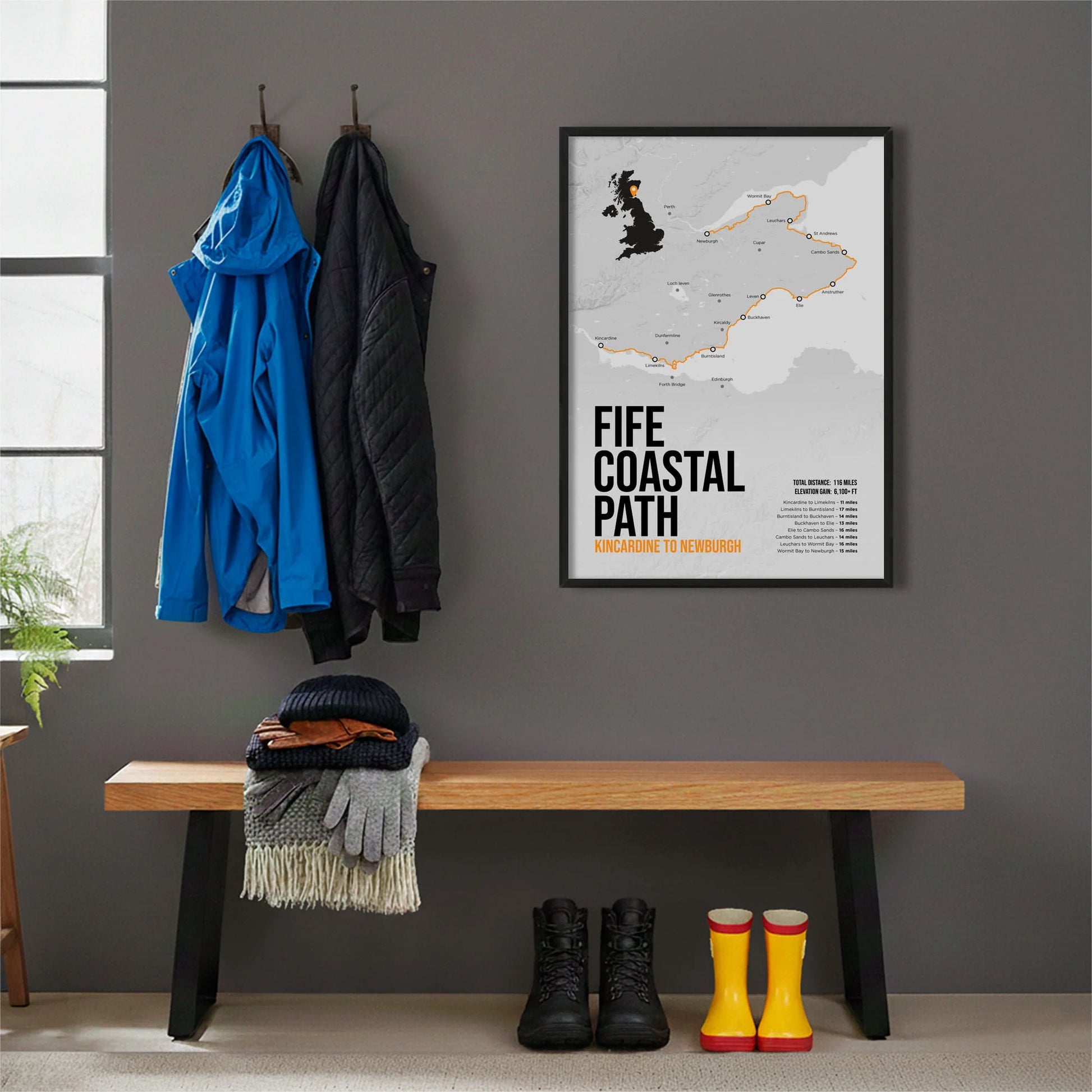 Framed print hanging on grey wall beside coats hanging above bench with walking boots and a scarf