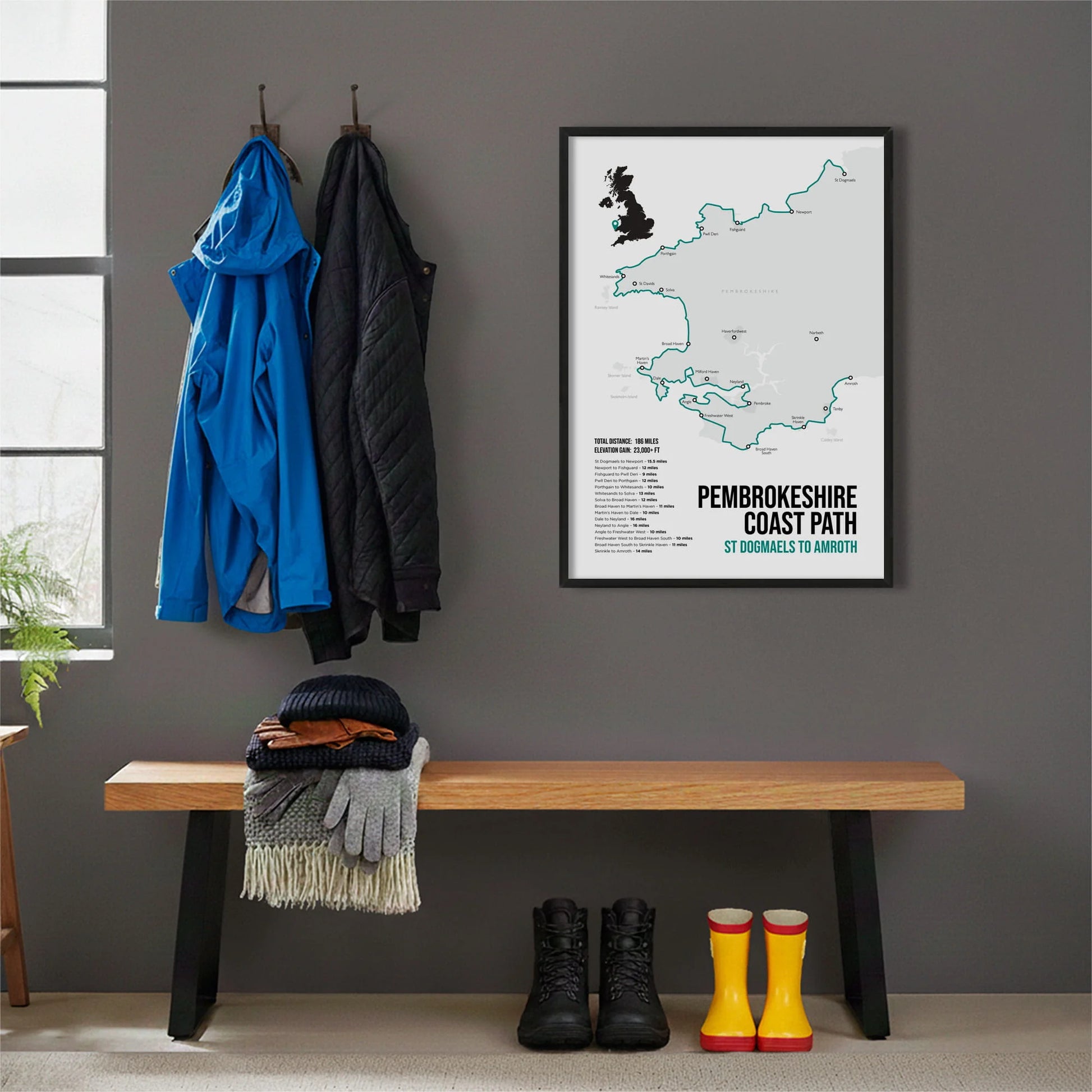 Framed print hanging on grey wall beside coats hanging above bench with walking boots and a scarf