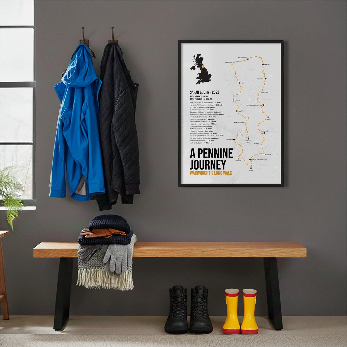 Framed print hanging on grey wall beside coats hanging above bench with walking boots and a scarf