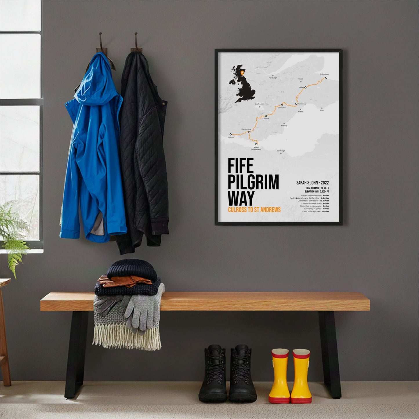 Framed print hanging on grey wall beside coats hanging above bench with walking boots and a scarf
