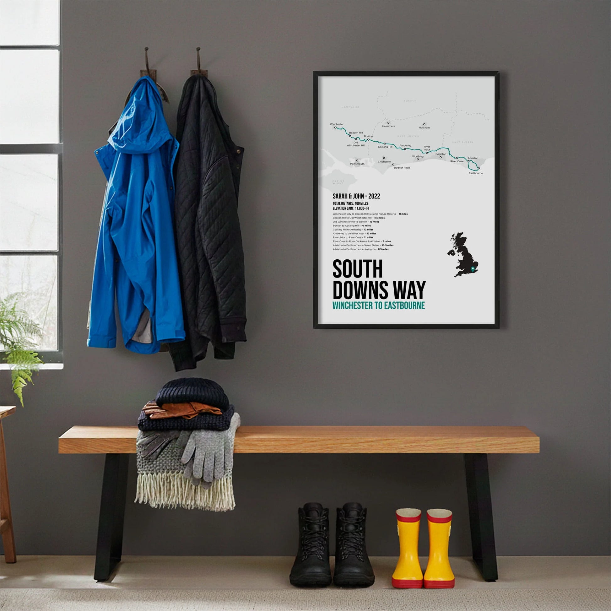 Framed print hanging on grey wall beside coats hanging above bench with walking boots and a scarf