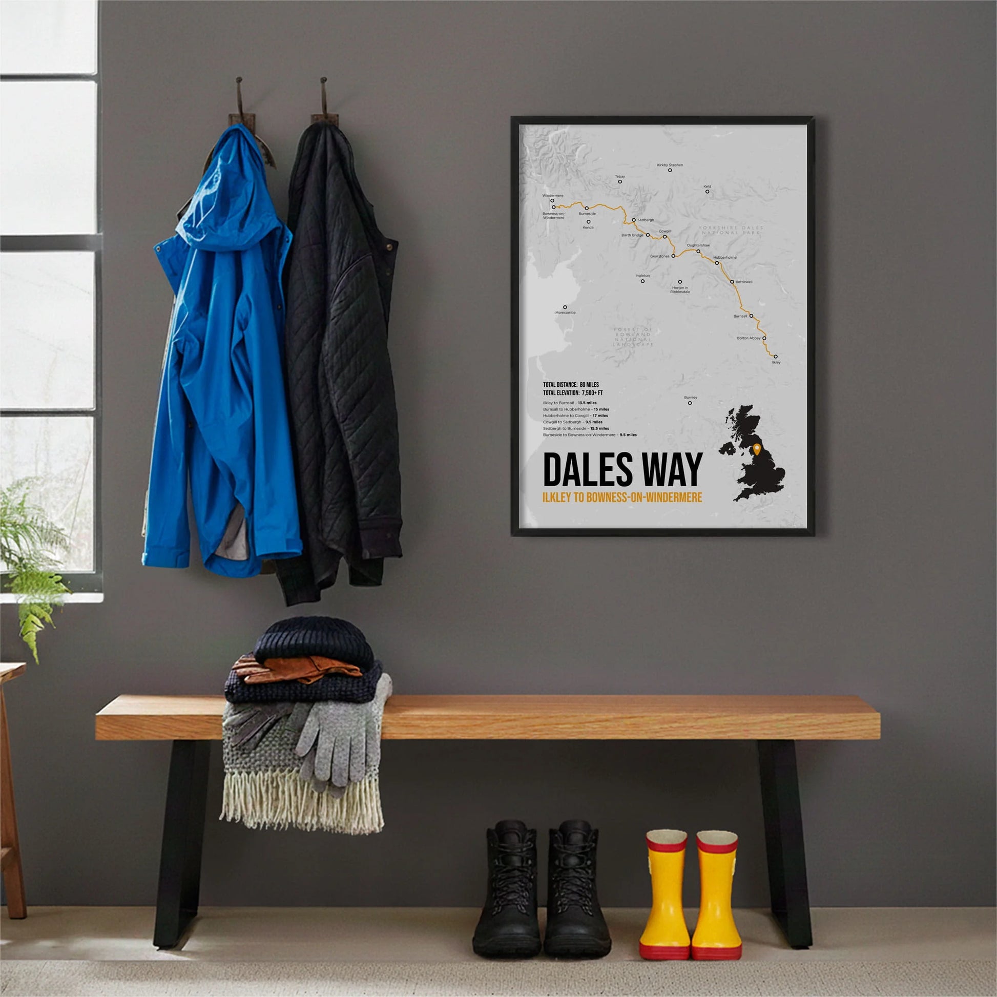 Framed print hanging on grey wall beside coats hanging above bench with walking boots and a scarf