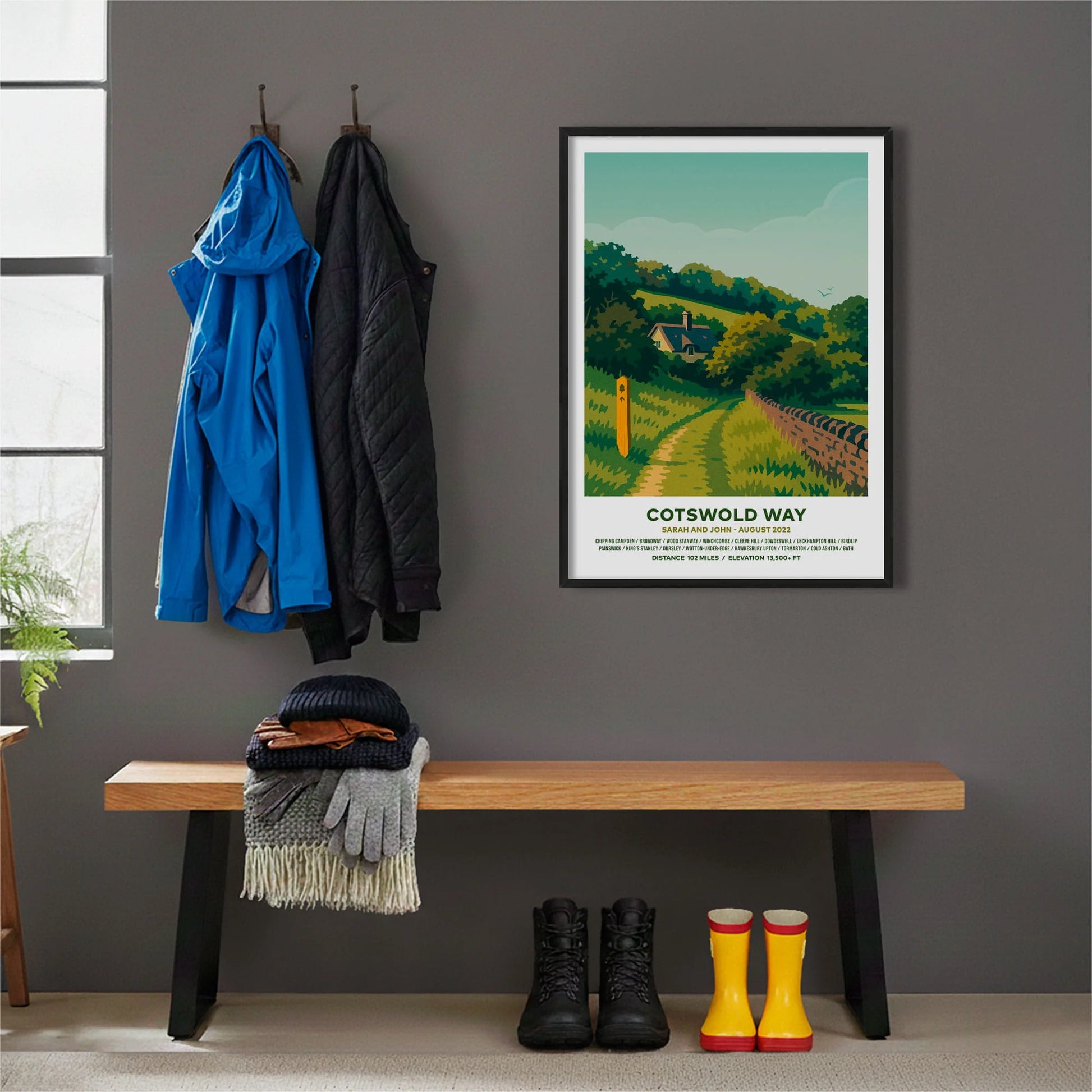 Framed print hanging on grey wall beside coats hanging above bench with walking boots and a scarf