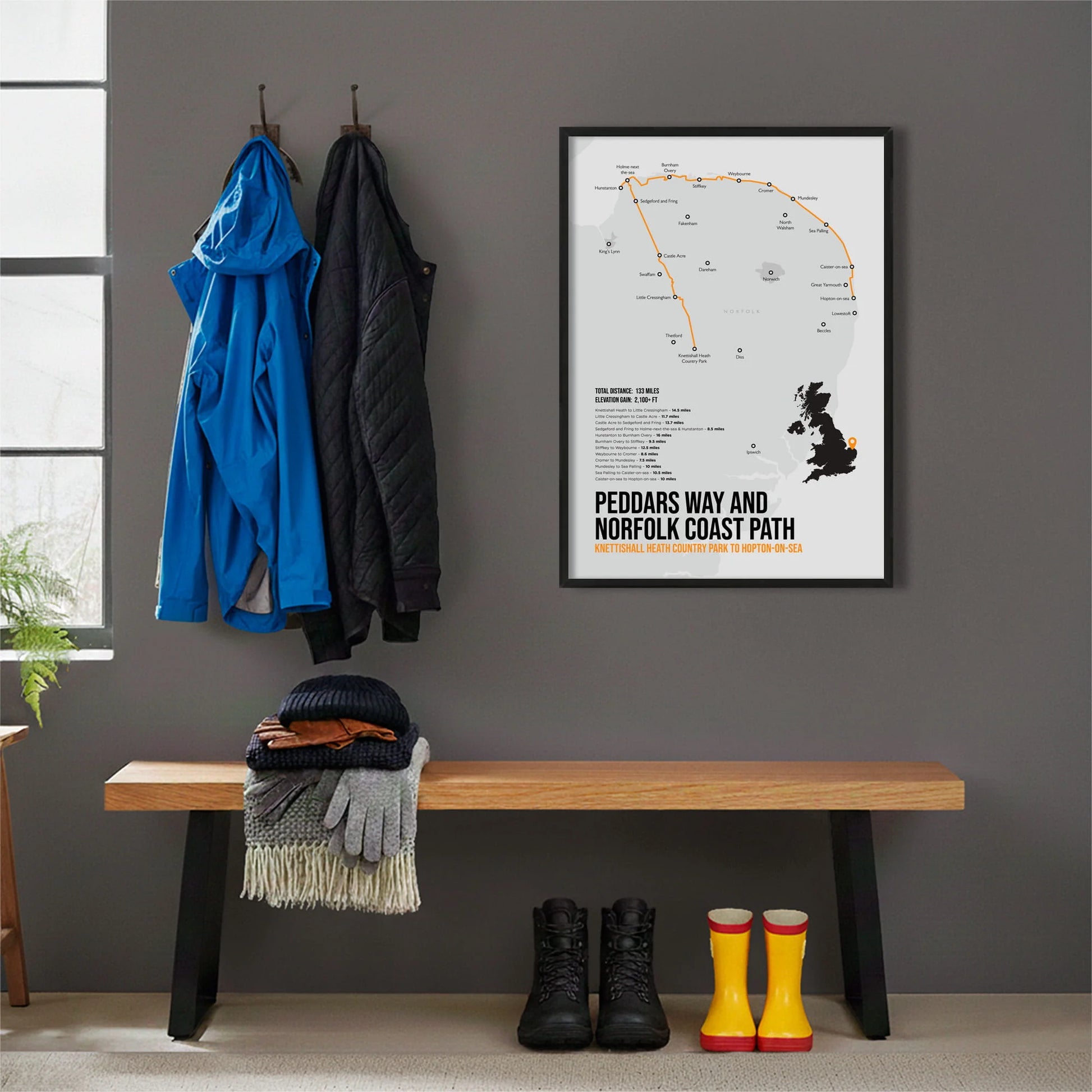 Framed print hanging on grey wall beside coats hanging above bench with walking boots and a scarf