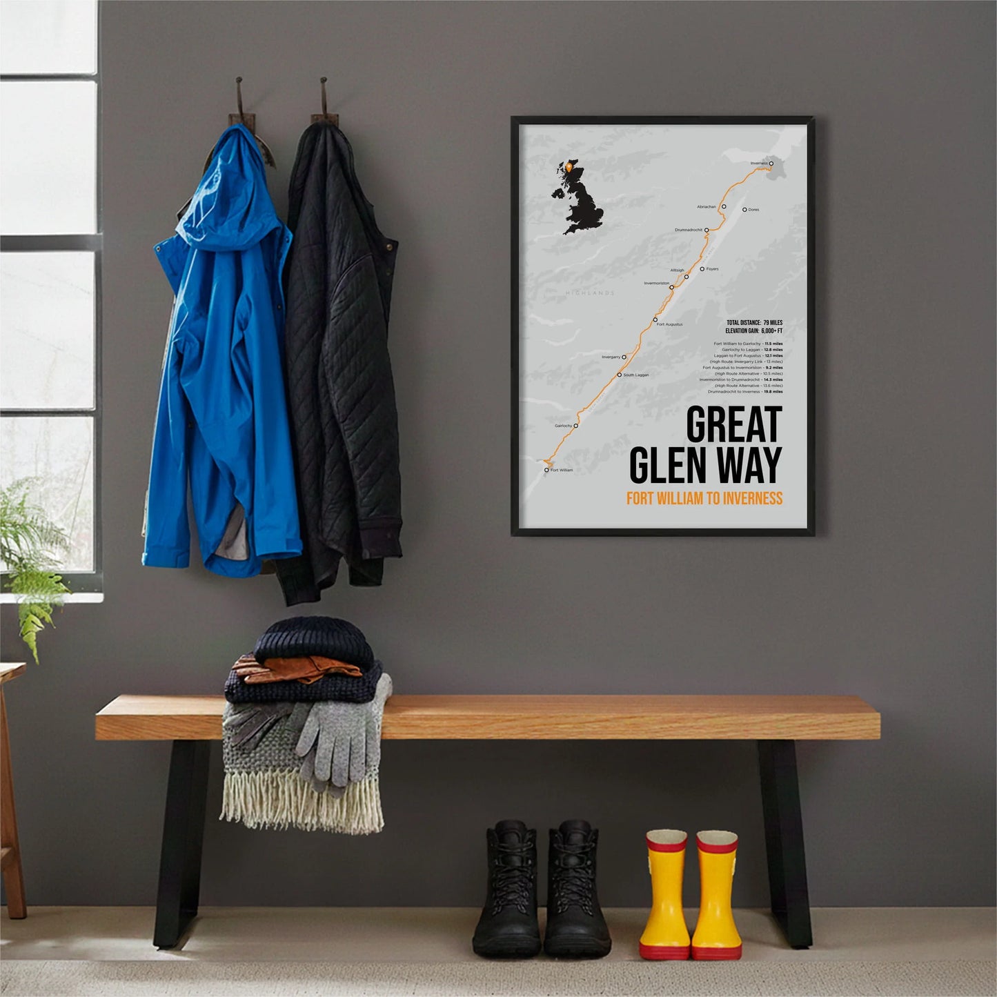Framed print hanging on grey wall beside coats hanging above bench with walking boots and a scarf