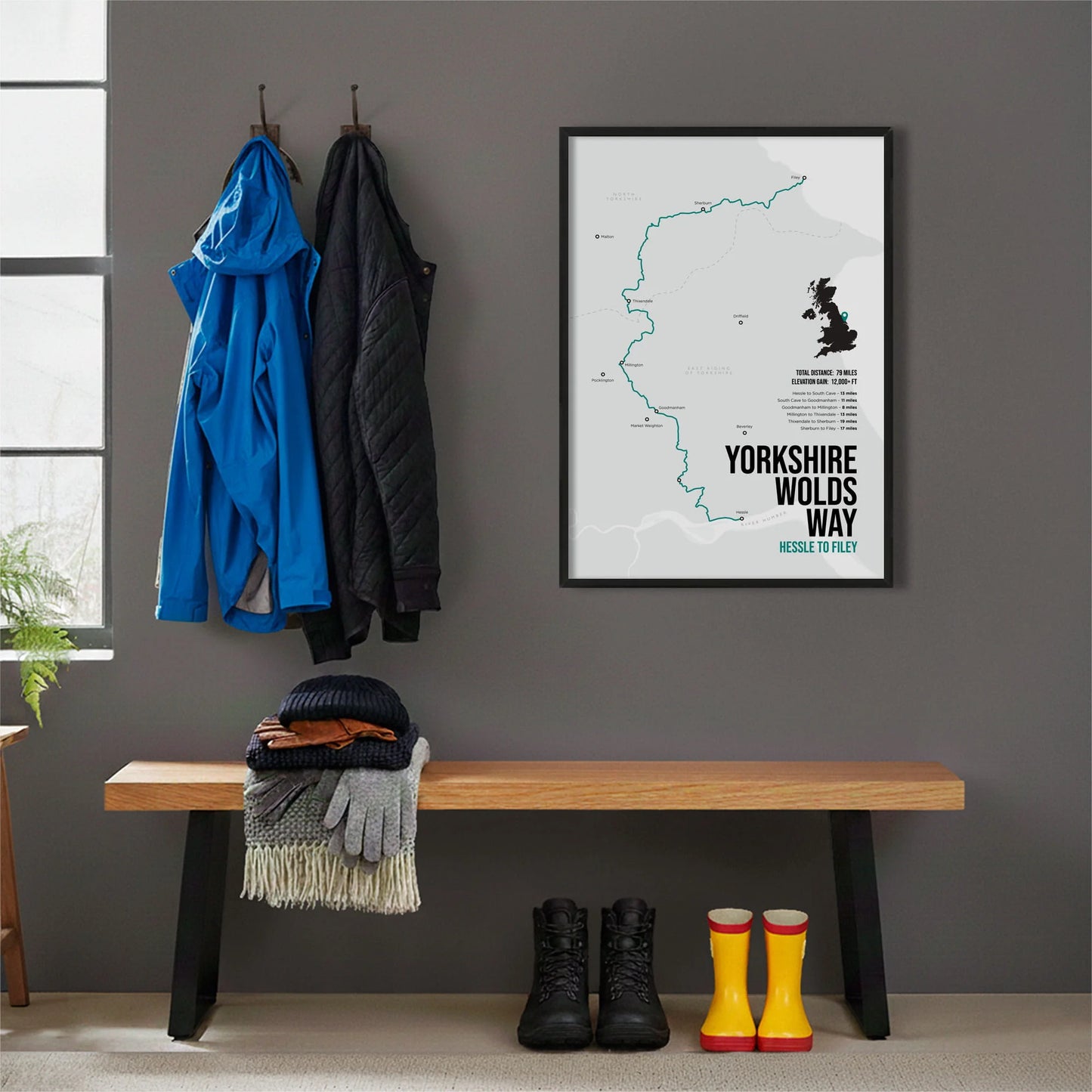 Framed print hanging on grey wall beside coats hanging above bench with walking boots and a scarf