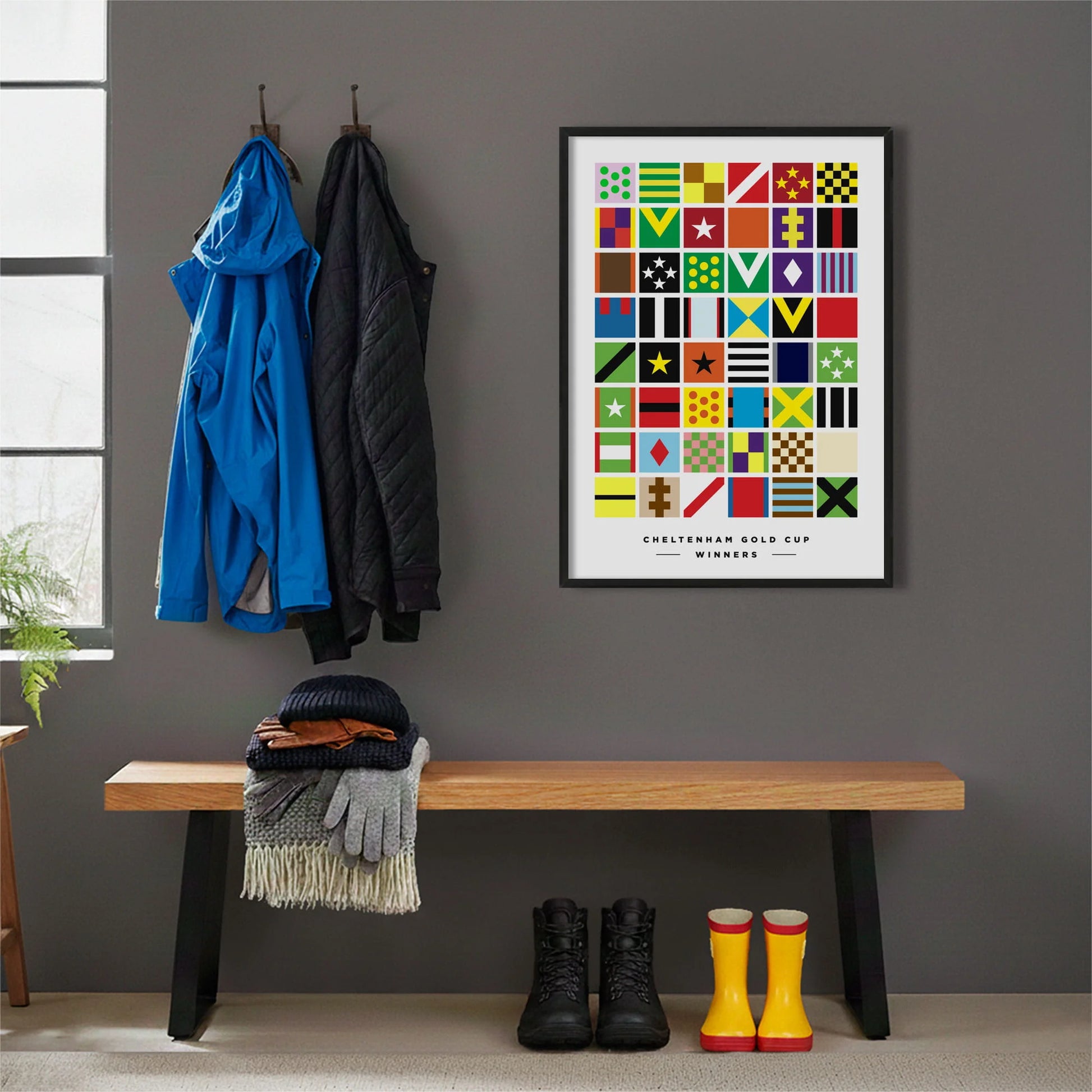Framed print hanging on grey wall beside coats hanging above bench with walking boots and a scarf